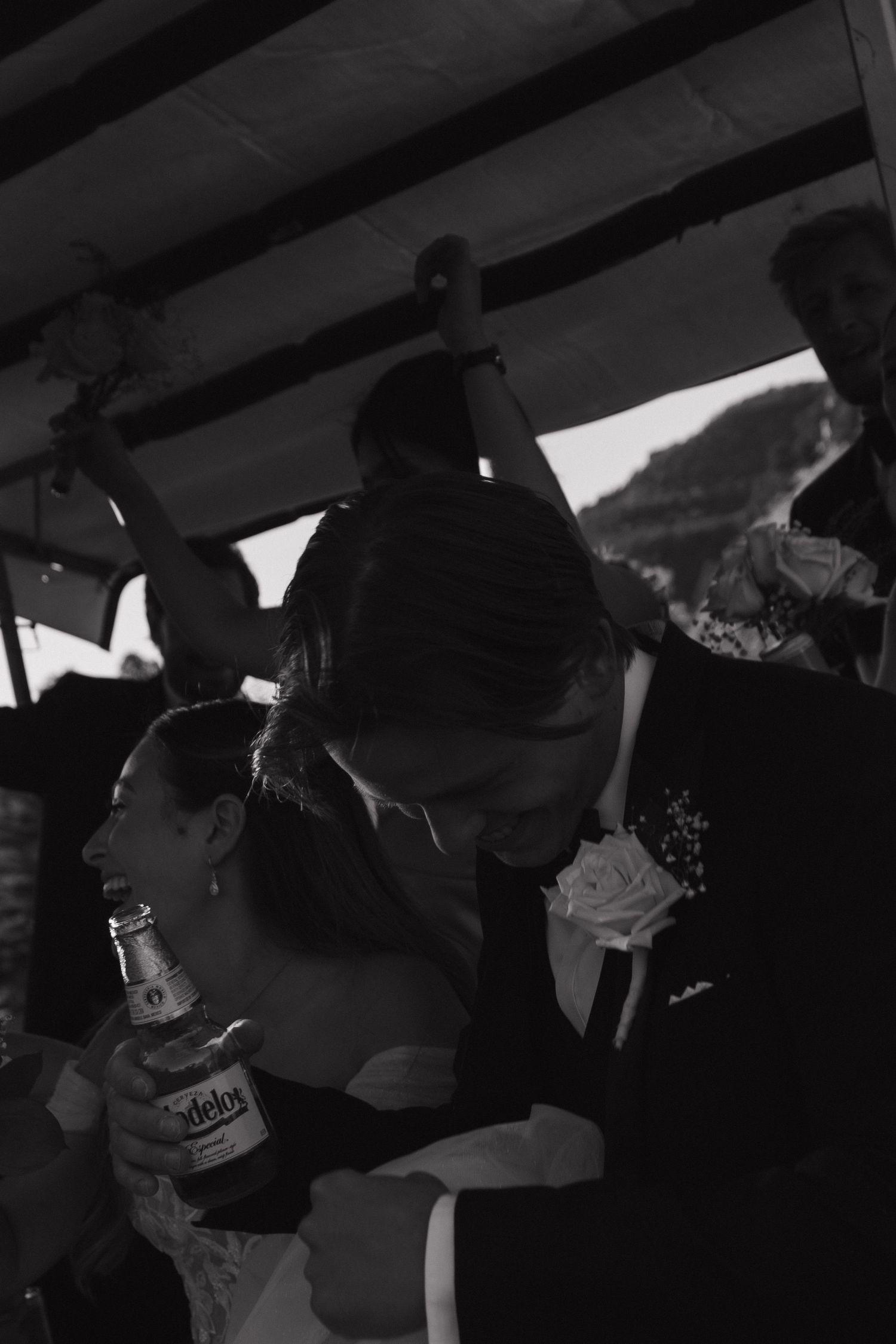 A black and white candid photo of a wedding reception with guests gathered under a covered venue.