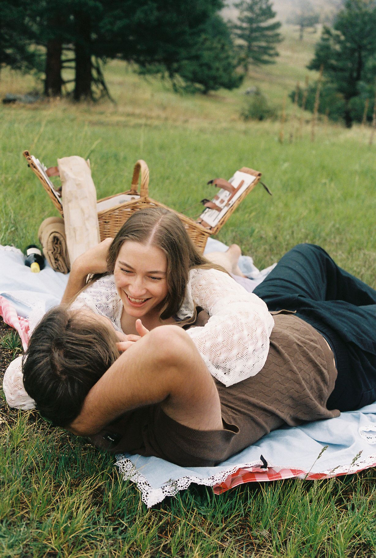 Happy couple lying on a picnic blanket in a grassy meadow, smiling and gazing at each other.