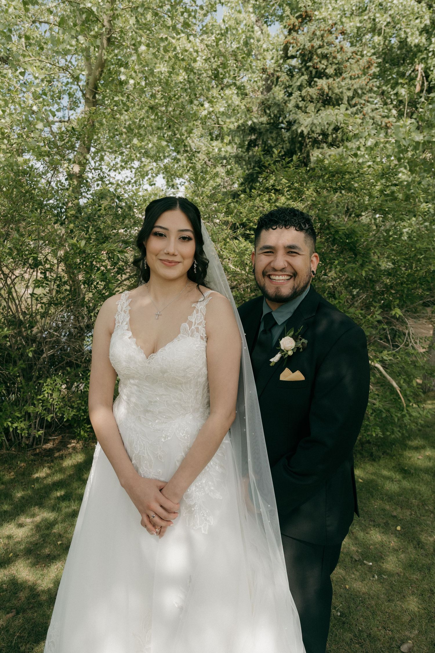 Bride and groom smiling together outdoors in lush green garden setting on their wedding day.