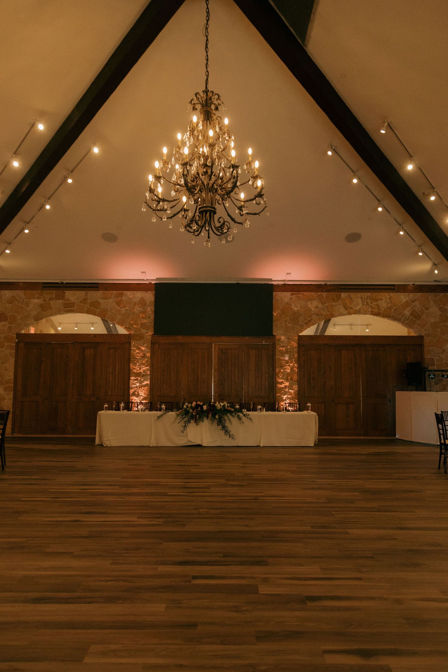 Elegant wedding reception hall with chandelier, vaulted ceiling, and sweetheart table.