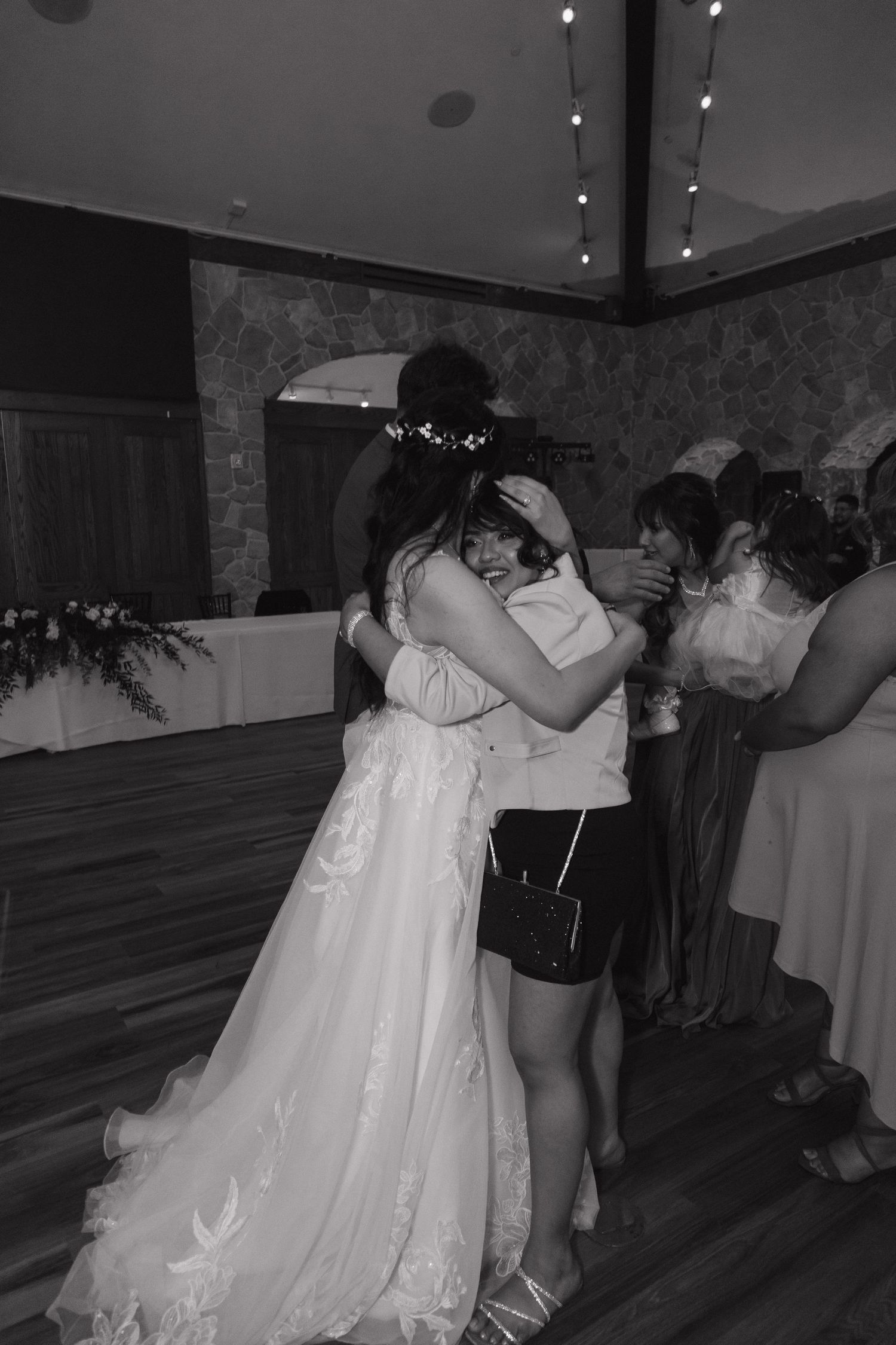 Bride shares a warm embrace with a guest on the wedding reception dance floor in black and white.