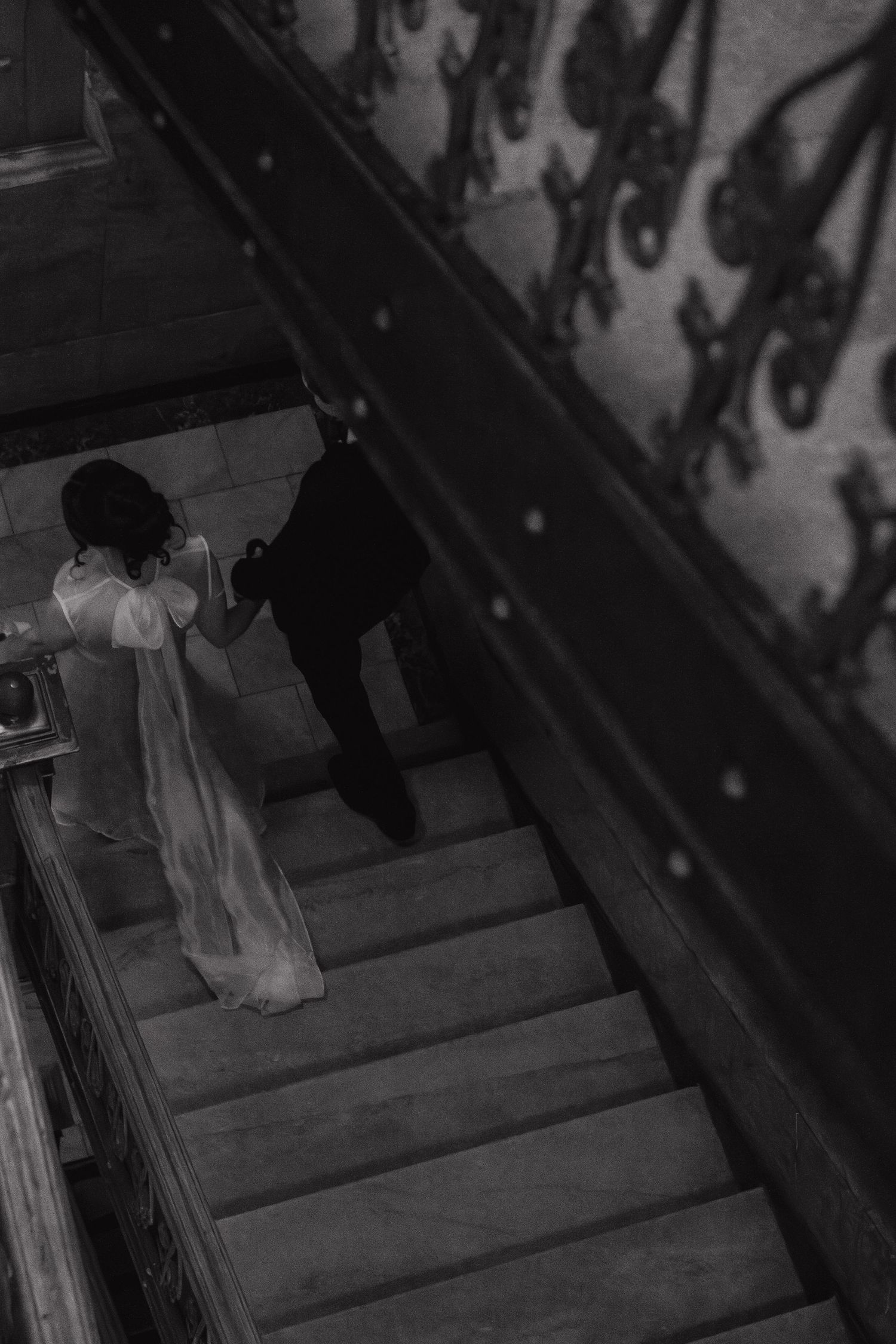 Couple descending an elegant staircase in formal attire, captured in black and white.