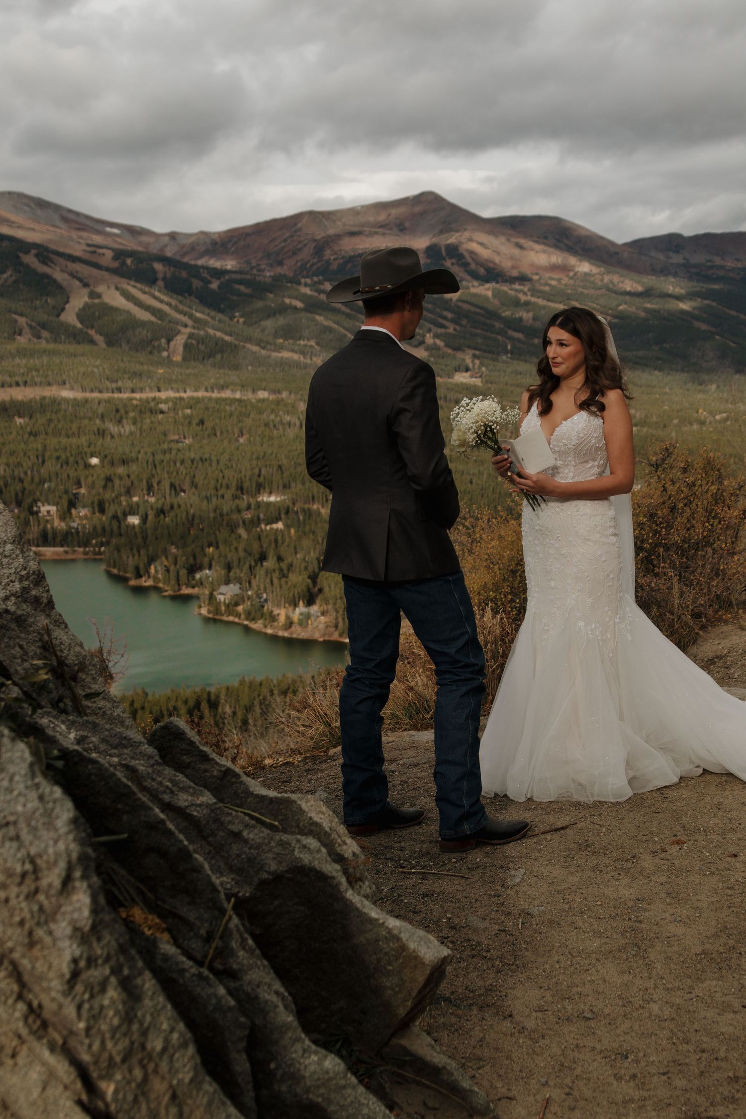 A scenic mountain wedding portrait overlooking a turquoise lake and rolling hills.