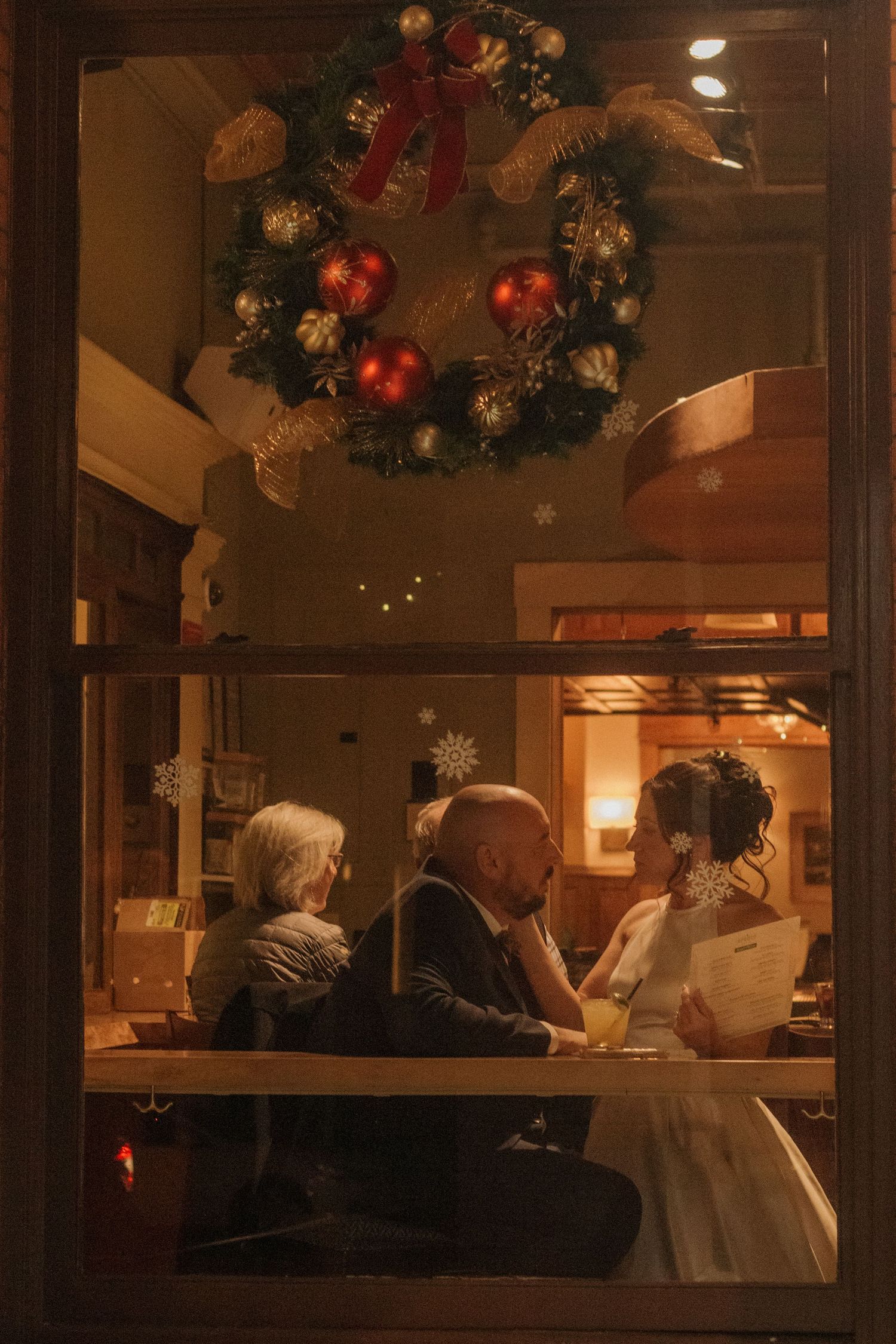 A wedding reception through a window at night with Christmas decorations and twinkling lights creating a festive ambiance.