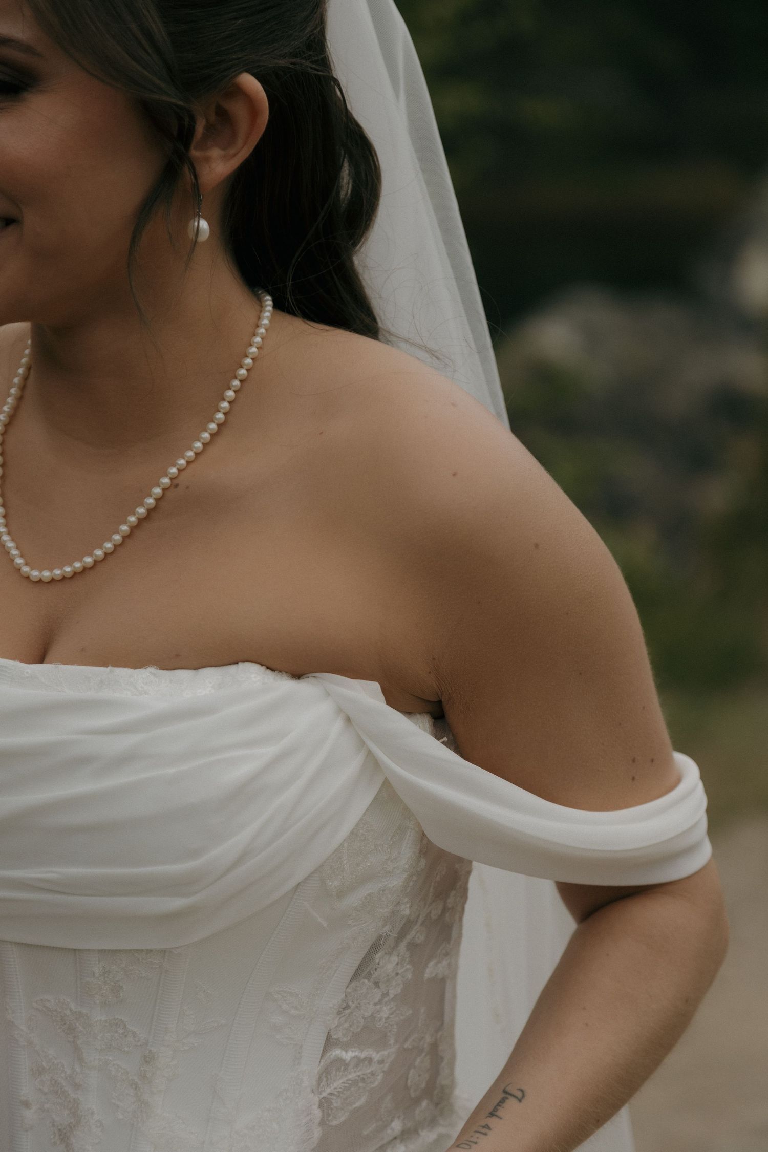 Close-up of bride in off-shoulder white gown with pearl necklace and veil on wedding day.