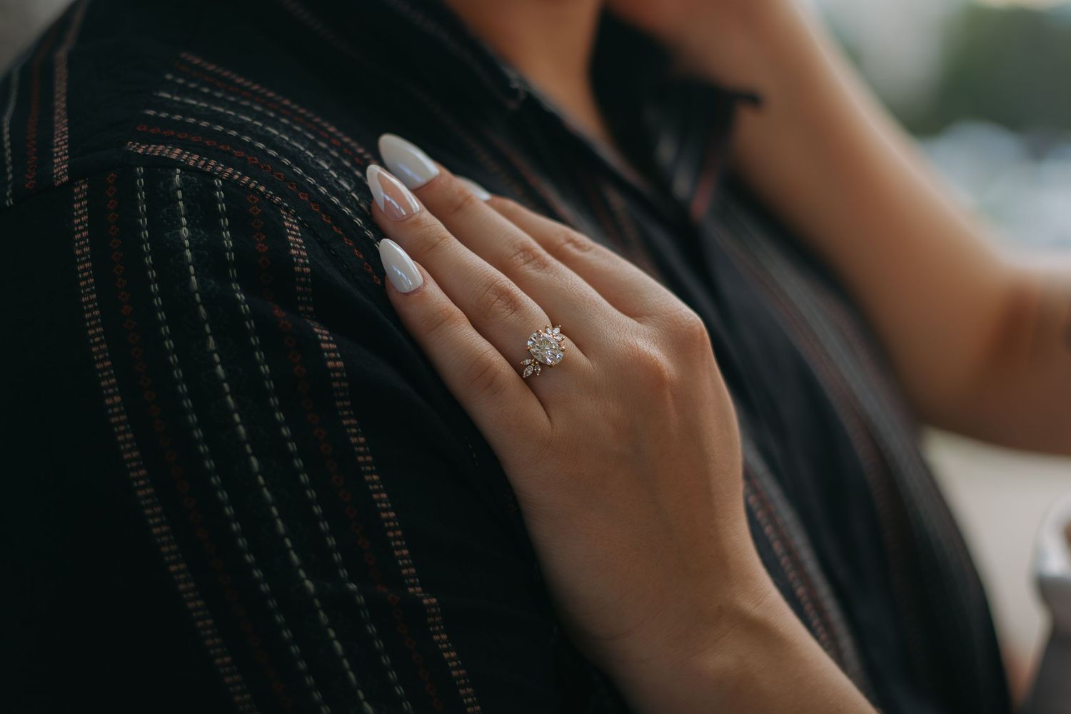 Close-up of a diamond engagement ring on a hand resting against a dark shirt.