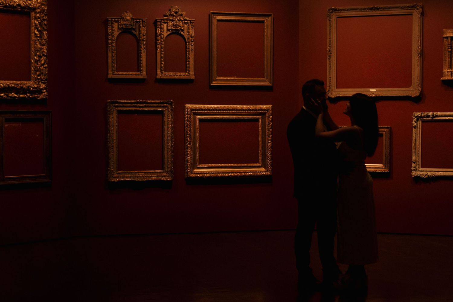 Dark atmospheric scene in museum gallery with multiple framed artworks on burgundy walls.