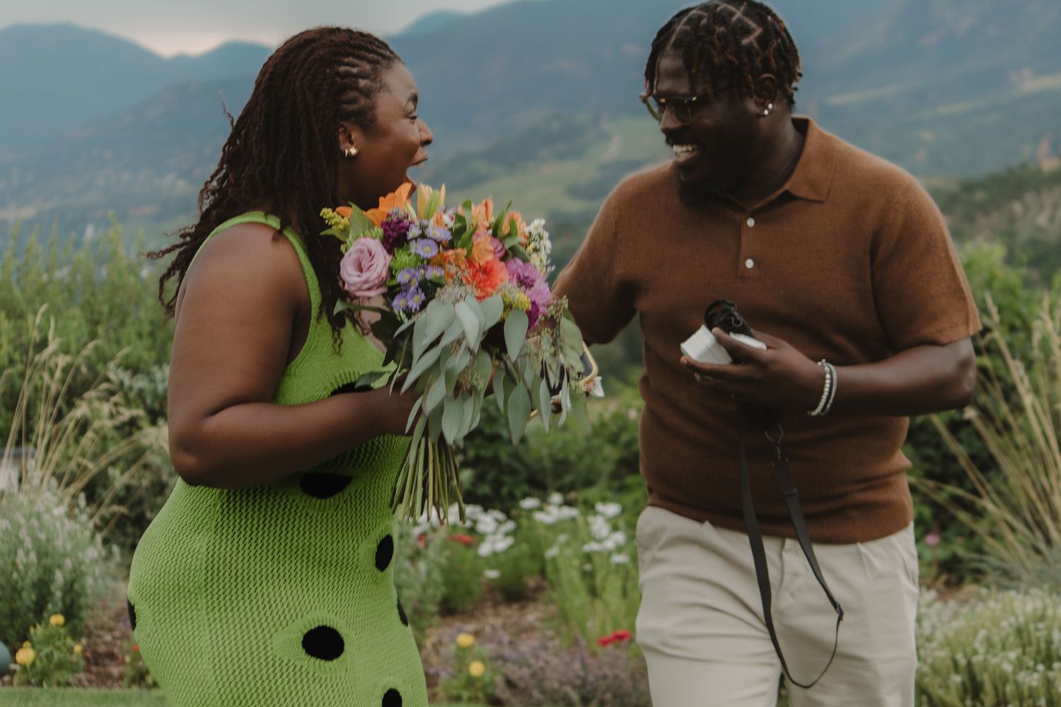 A candid moment shared between two individuals with a colorful bouquet against mountain scenery.