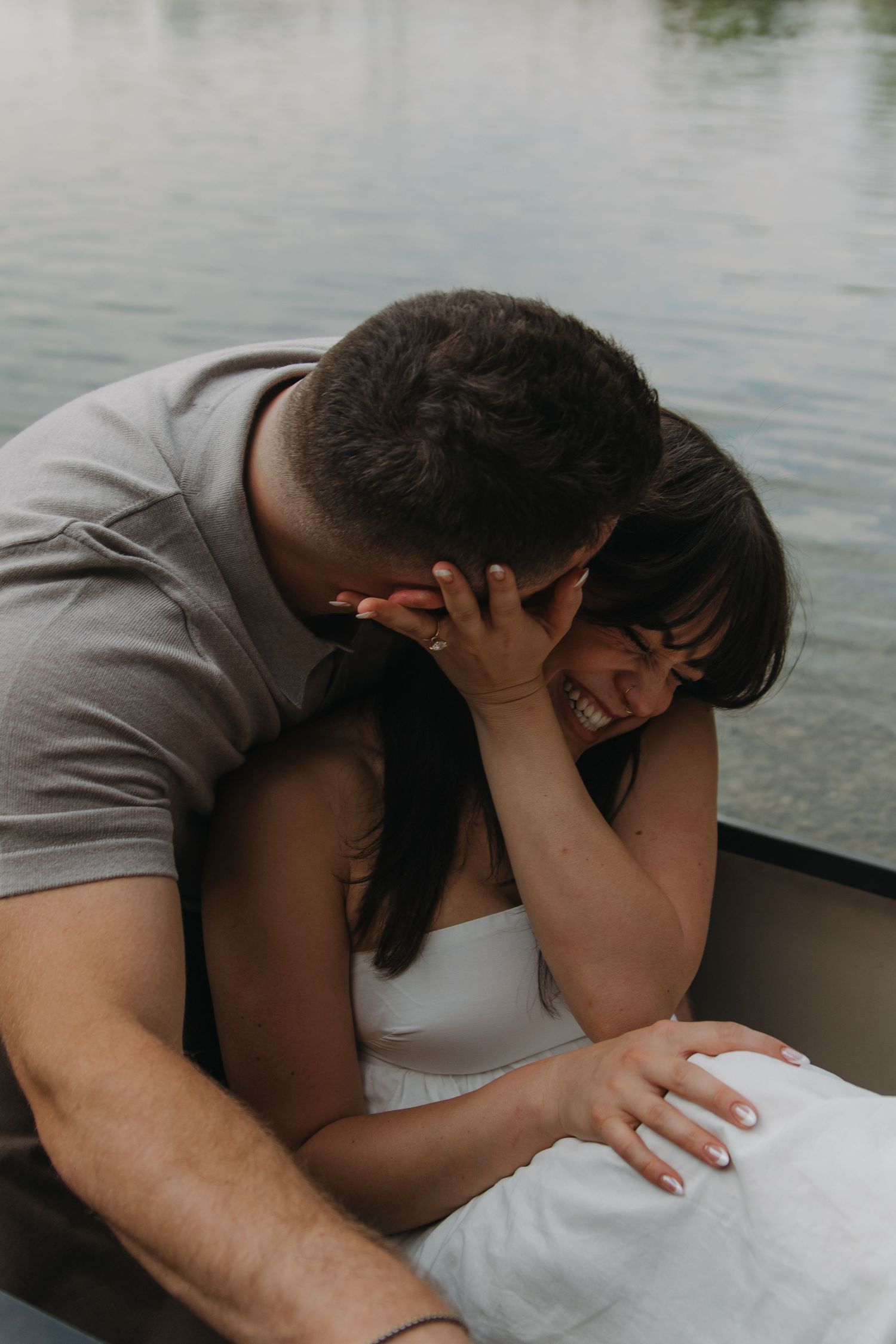 A romantic couple laughing and embracing while sitting in a boat on calm waters during an intimate moment.