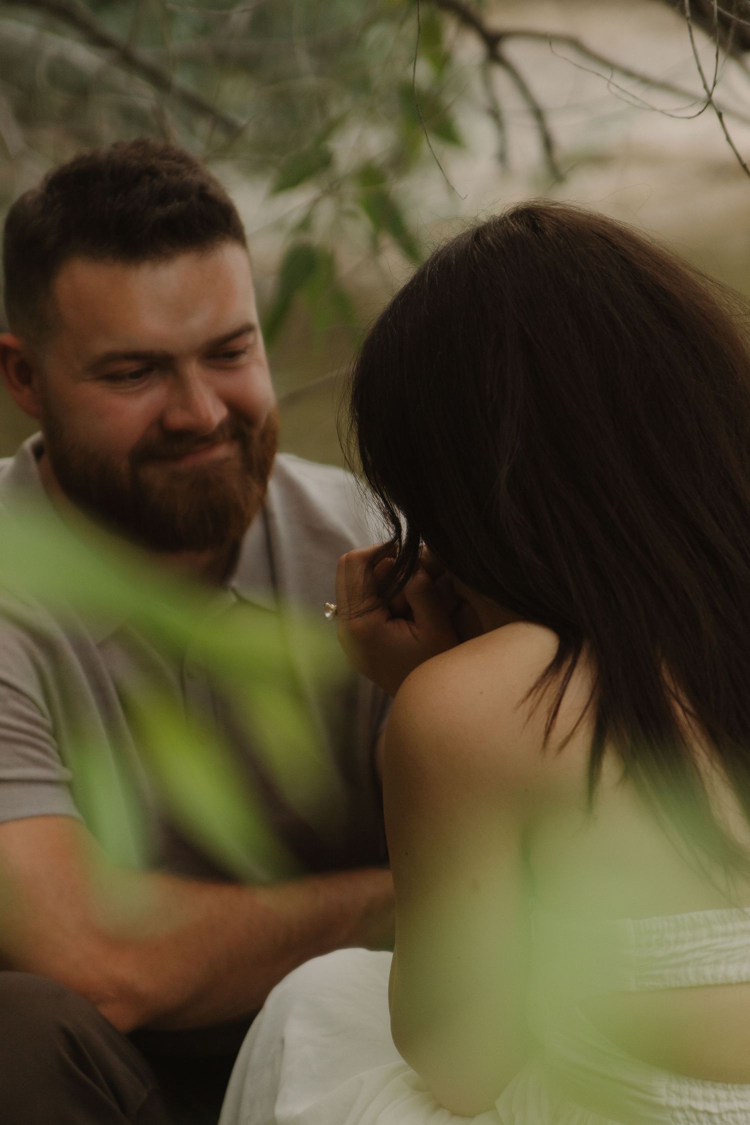Intimate couple's photoshoot through green foliage by the water.