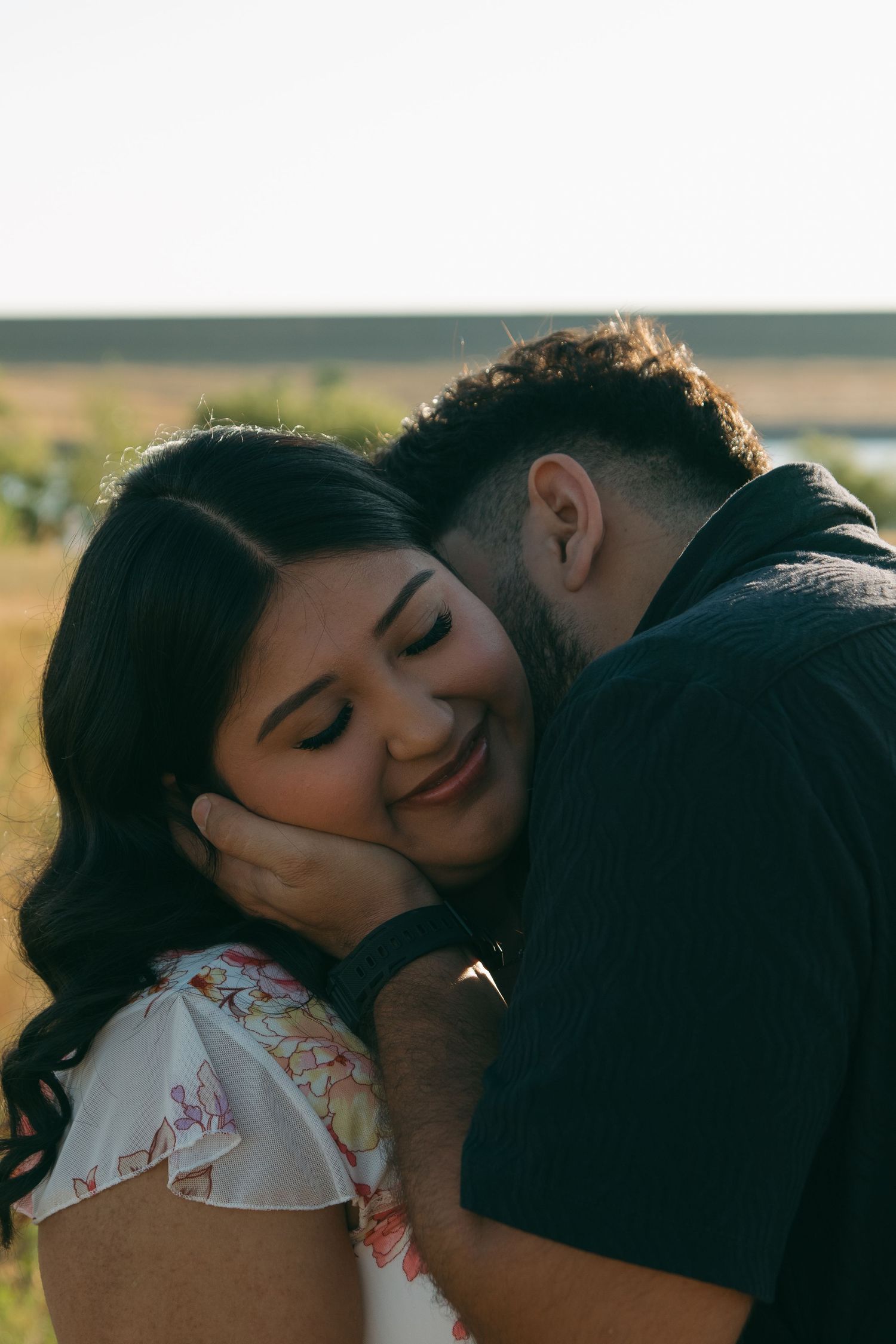 A romantic sunset photoshoot in a field with a couple in embrace wearing black and floral dress.