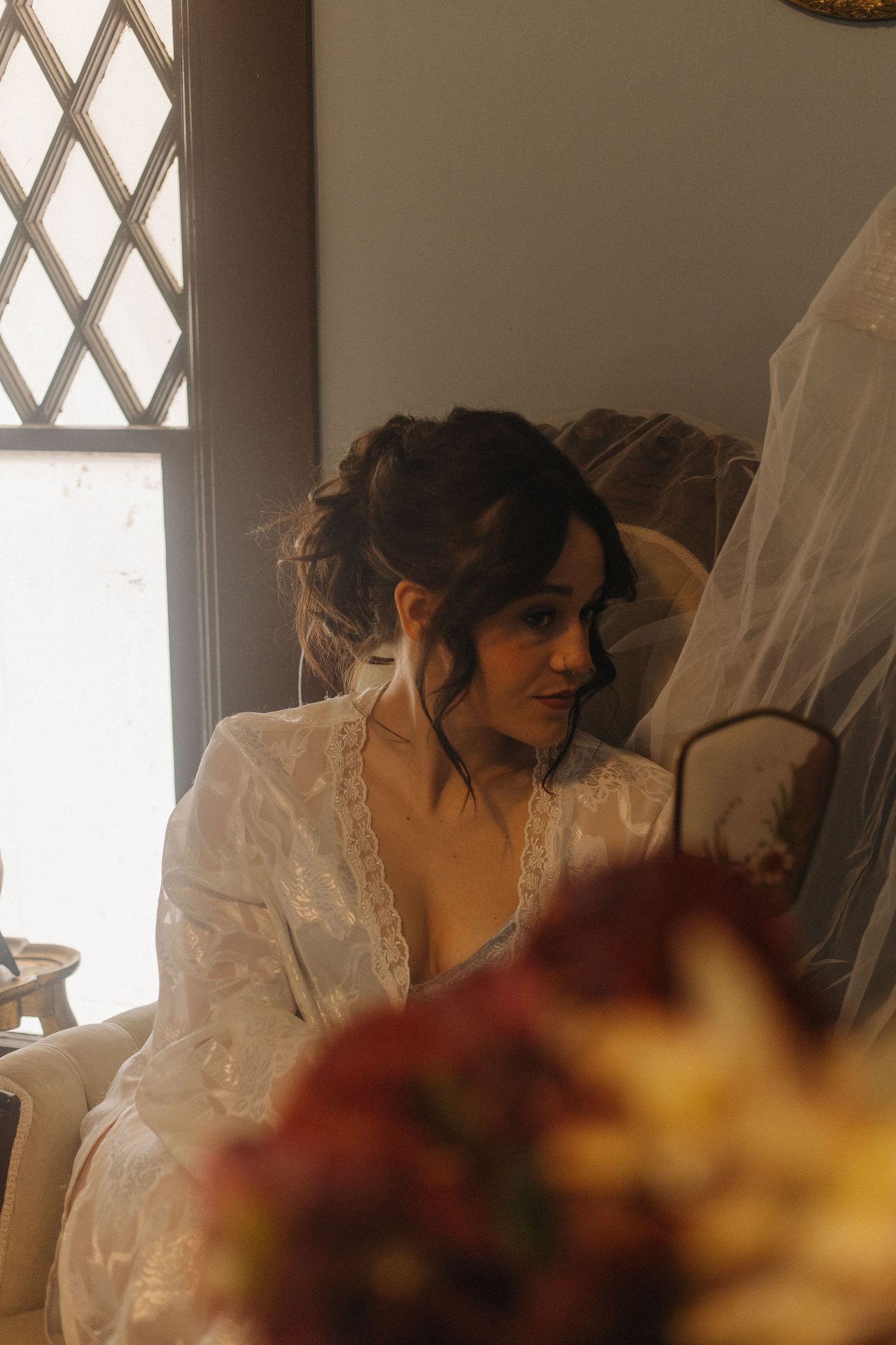 Soft natural light streams through window as bride prepares in lace details.