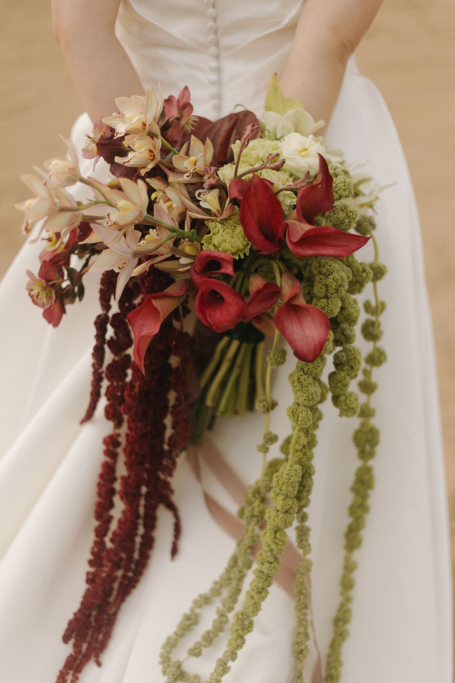 Close-up of cascading burgundy and green floral bouquet against white wedding dress.