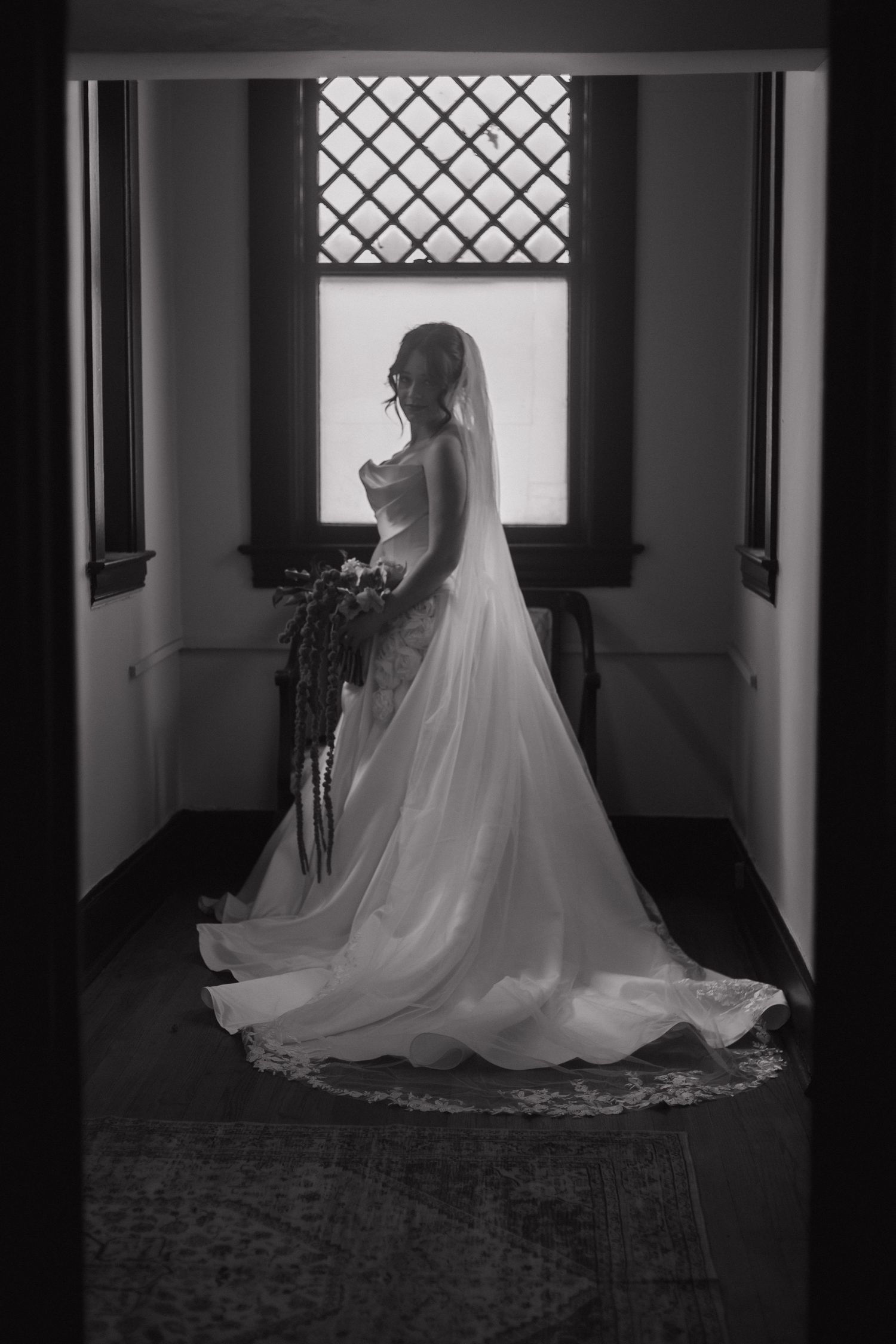 Dramatic black and white silhouette of wedding dress and veil in historic hallway.