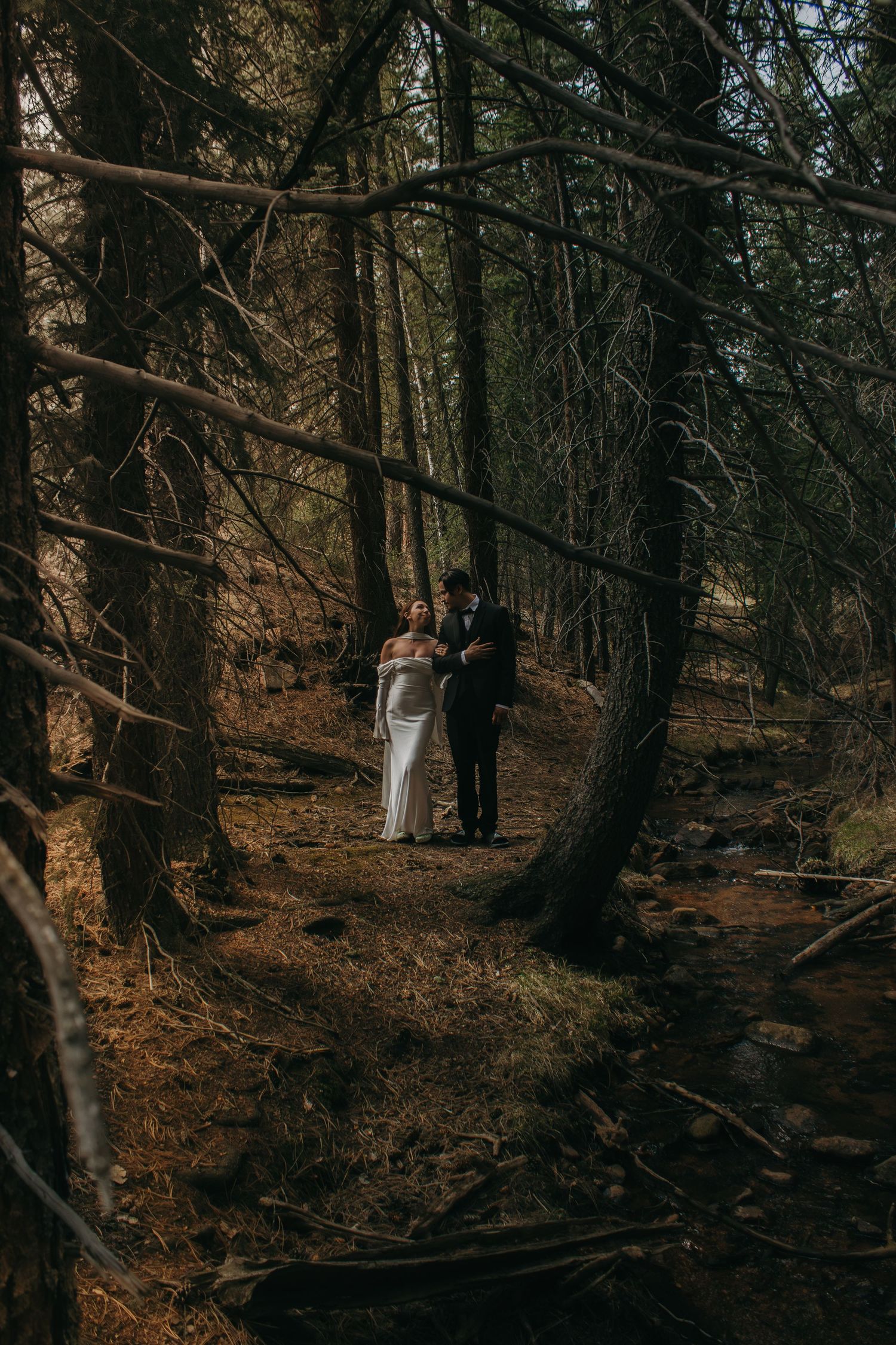 A couple in wedding attire walking along a romantic forest trail.