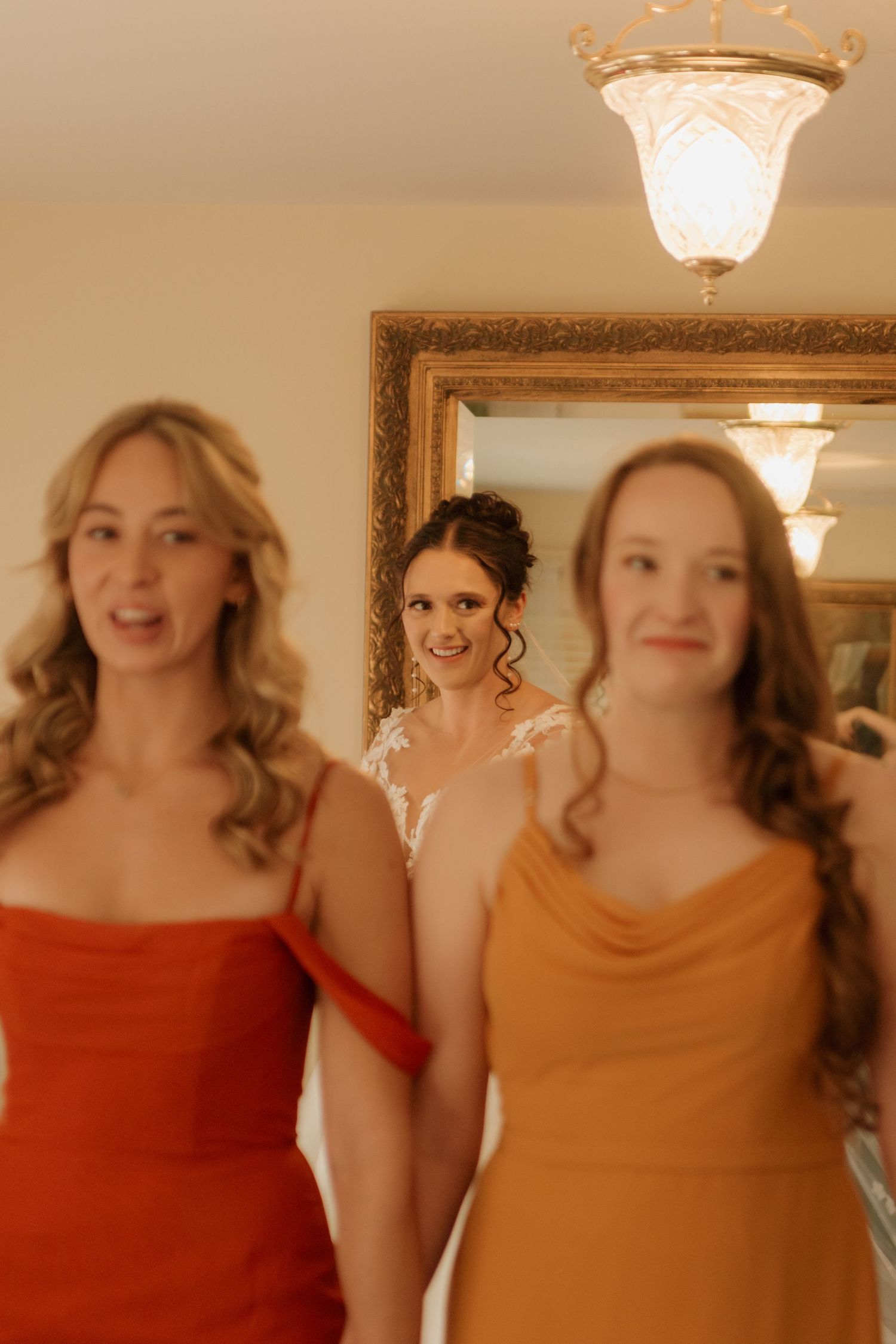 Joyful wedding party members smiling under crystal chandeliers.