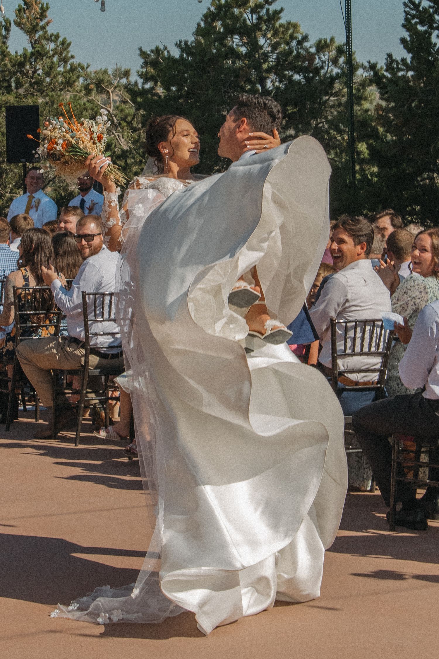 Bride's white dress flowing during celebratory dance moves at outdoor reception.