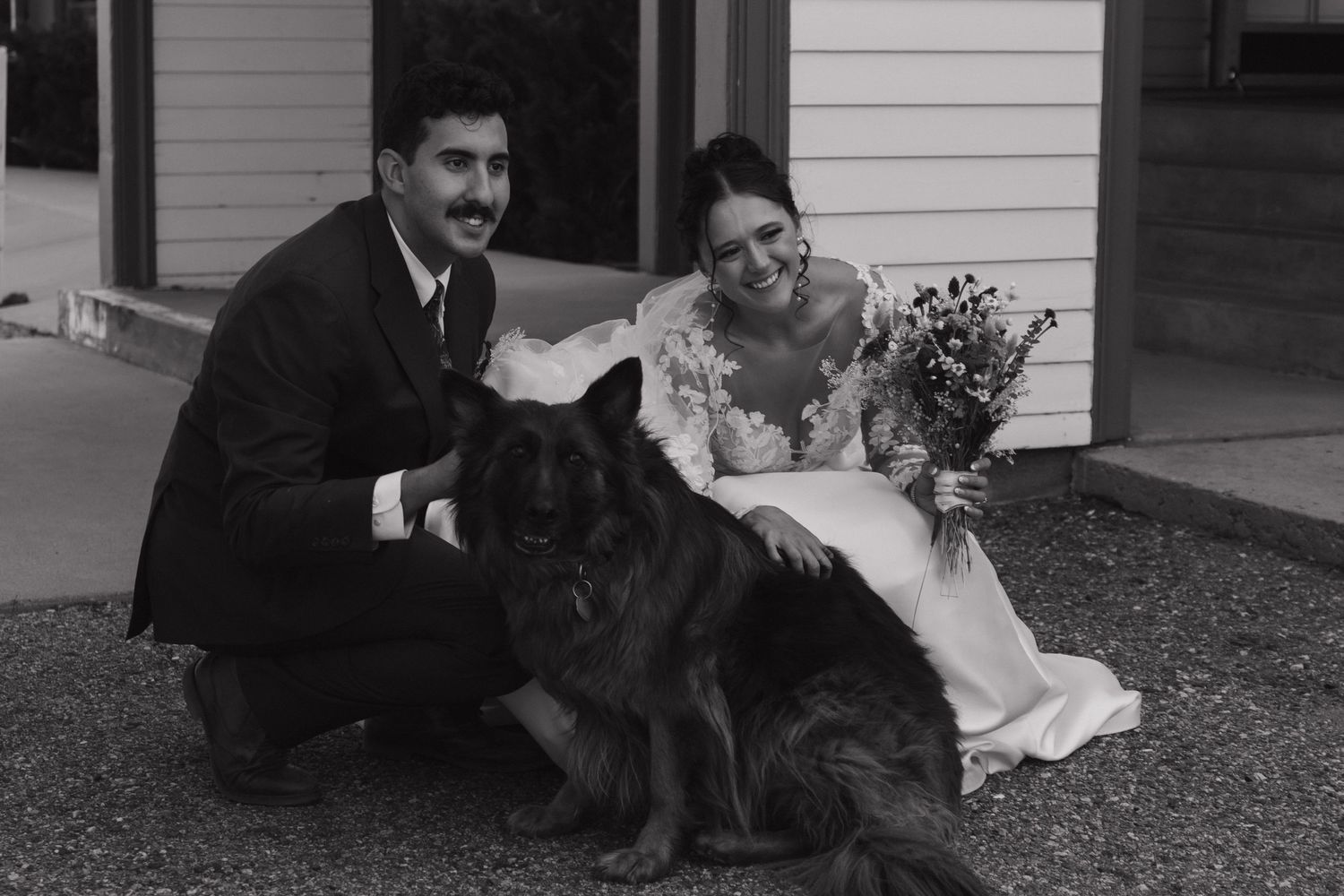 A couple poses with their dogs outside a white farmhouse on their wedding day.
