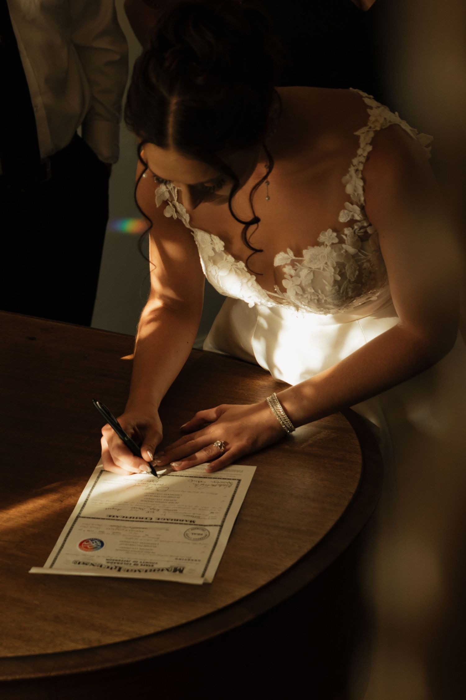 Close-up of wedding dress detail as document is signed in dramatic lighting.