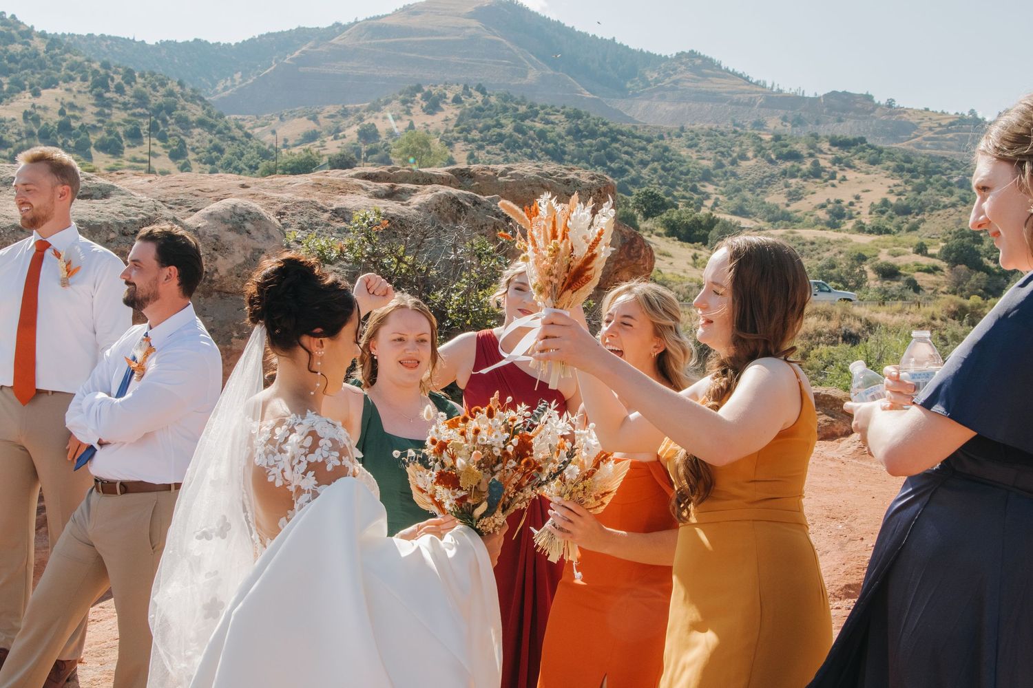 Wedding group portrait captured outdoors with mountains and natural scenery in the background.