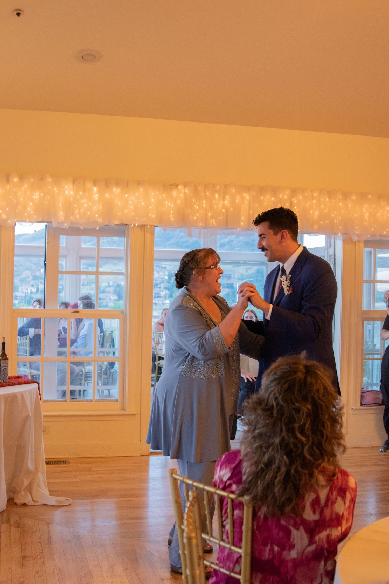 Wedding reception dancing in a warmly lit room with large windows.