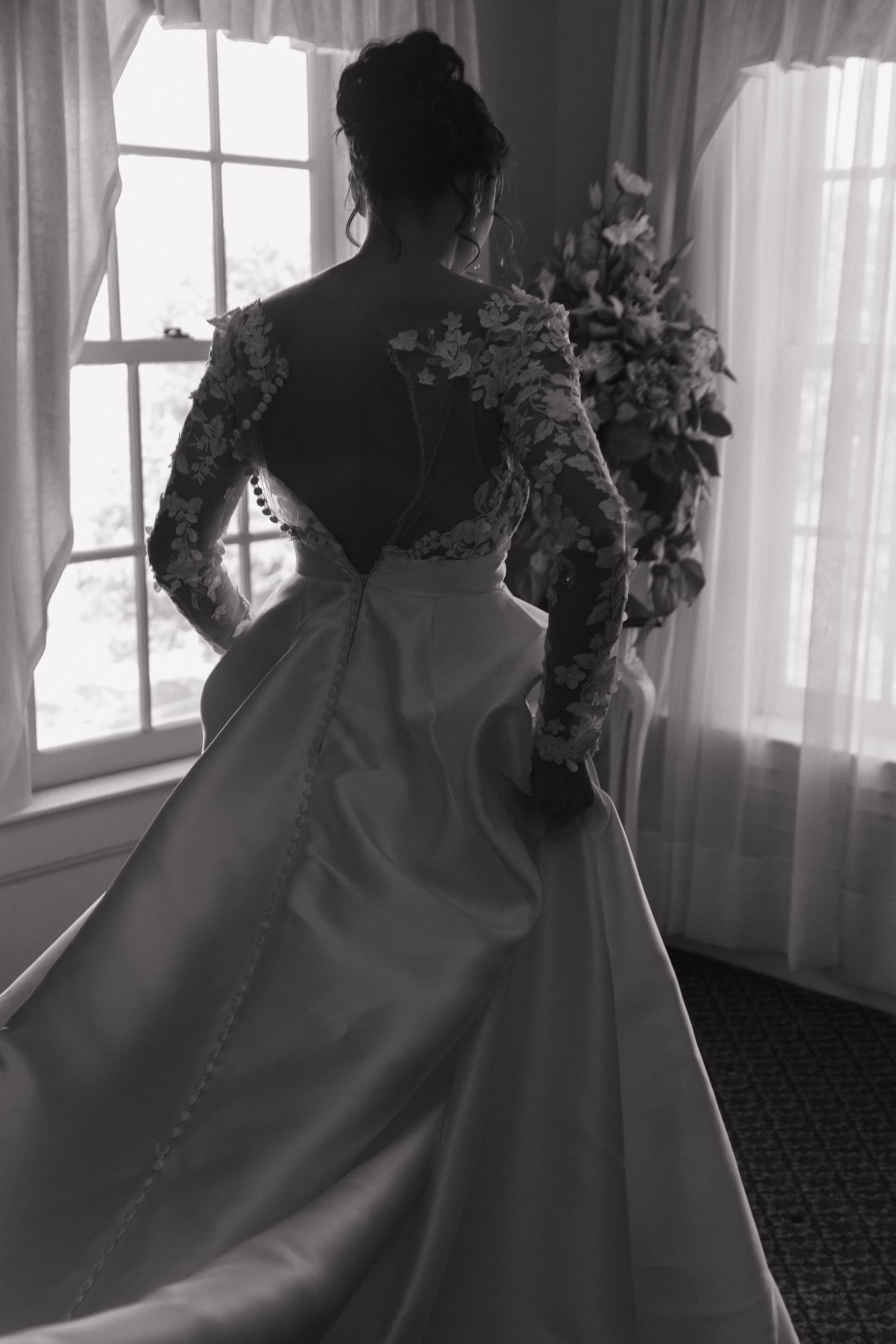 Elegant wedding dress train trailing on carpeted floor near sunlit windows.