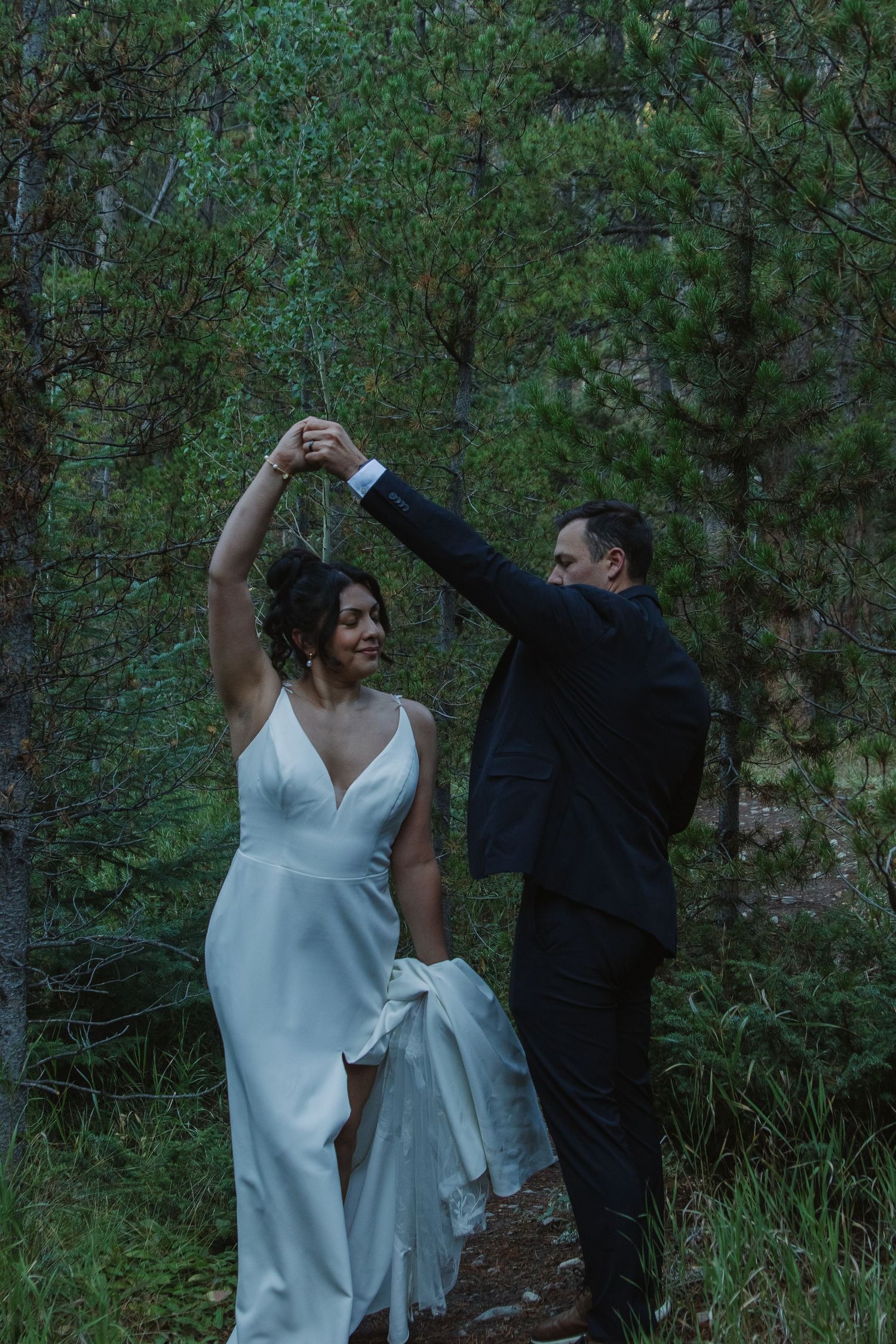 Couple dancing together in a natural wooded setting with the bride wearing a flowing white dress.