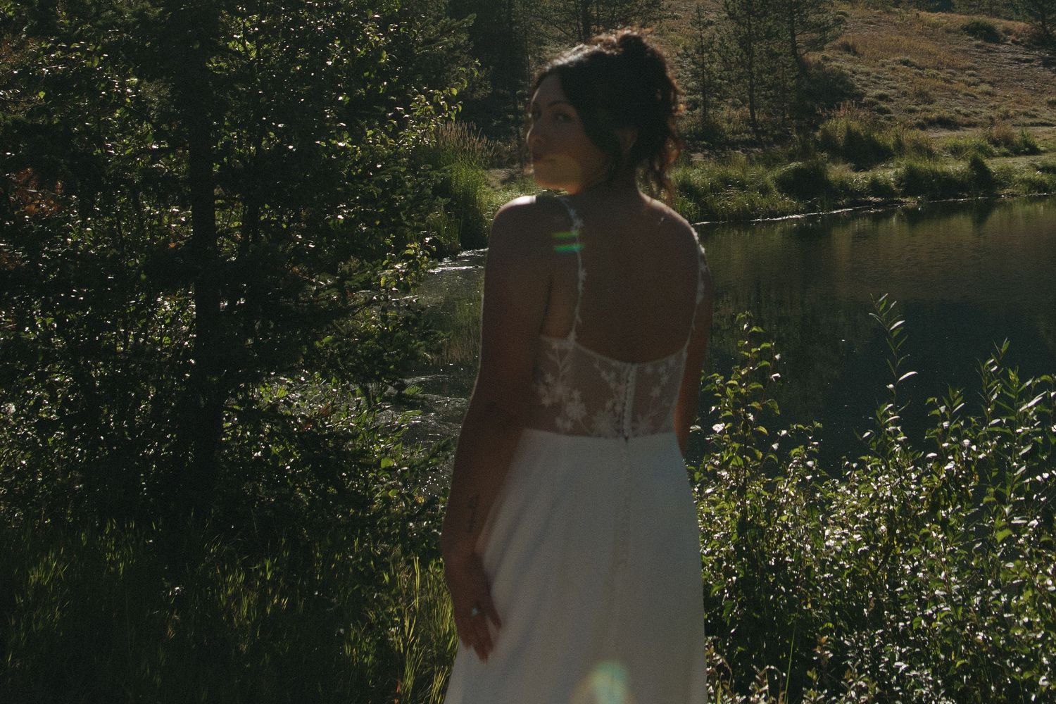 Wedding couple sharing tender moment by lake with mountain backdrop.
