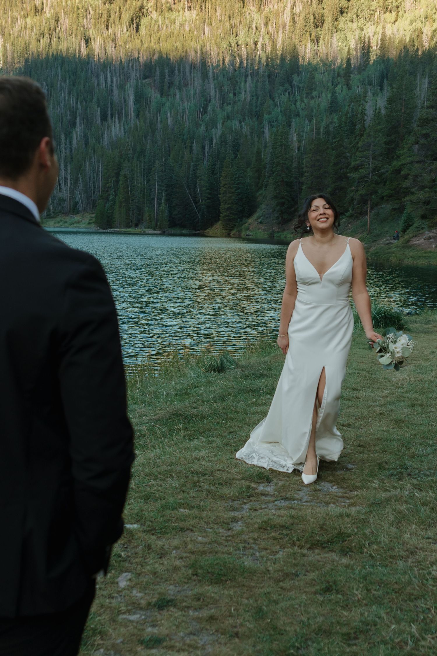 A couple shares playful moments on grassy lakeside terrain during their wedding photoshoot.