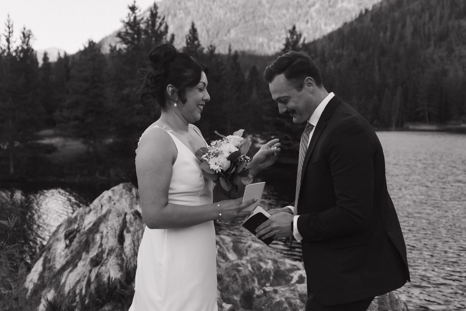 A romantic wedding ceremony takes place by a mountain lake with evergreen trees in the background.