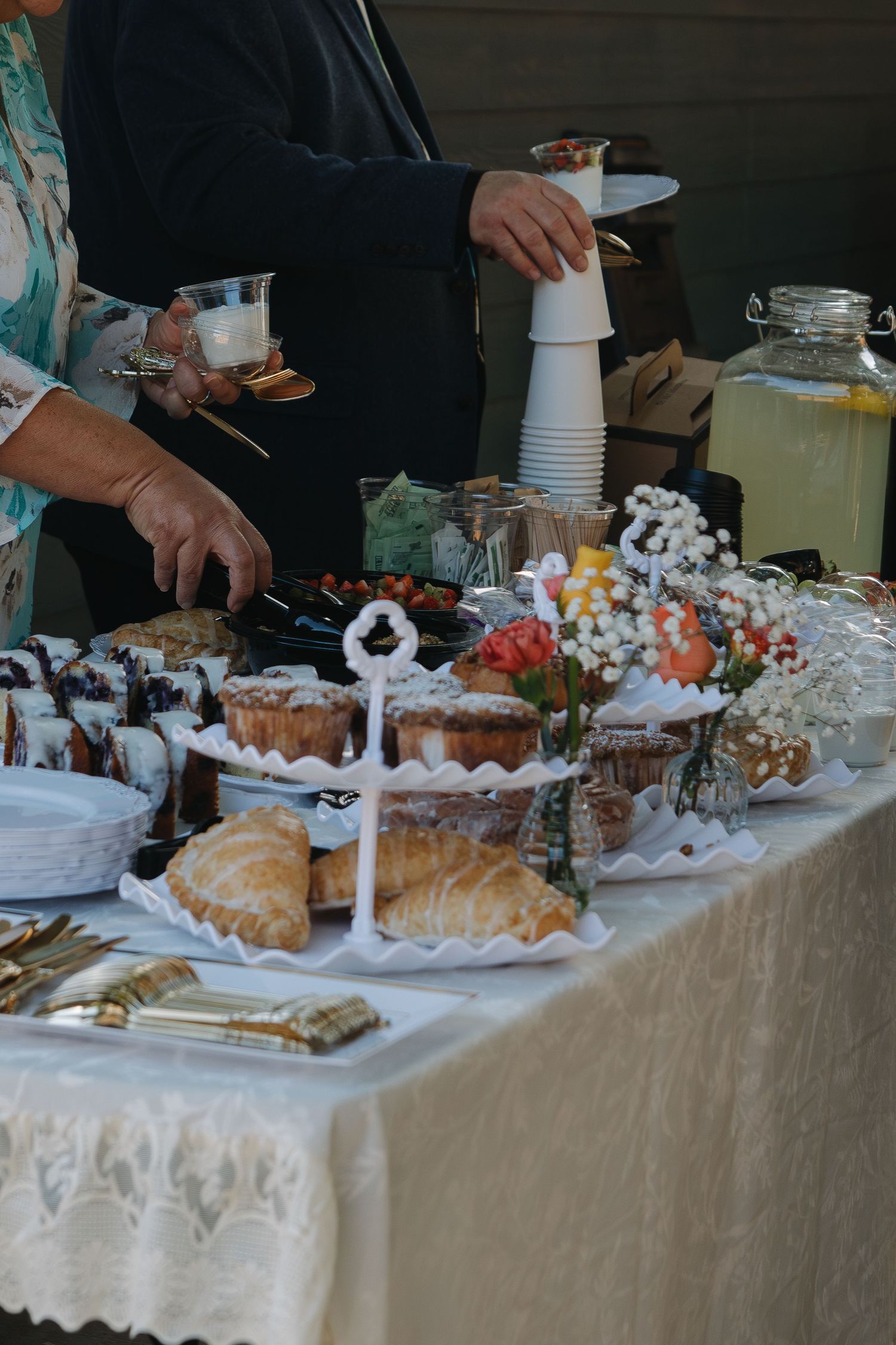A dessert buffet table laden with pastries and sweets on white tablecloths at a catered event.
