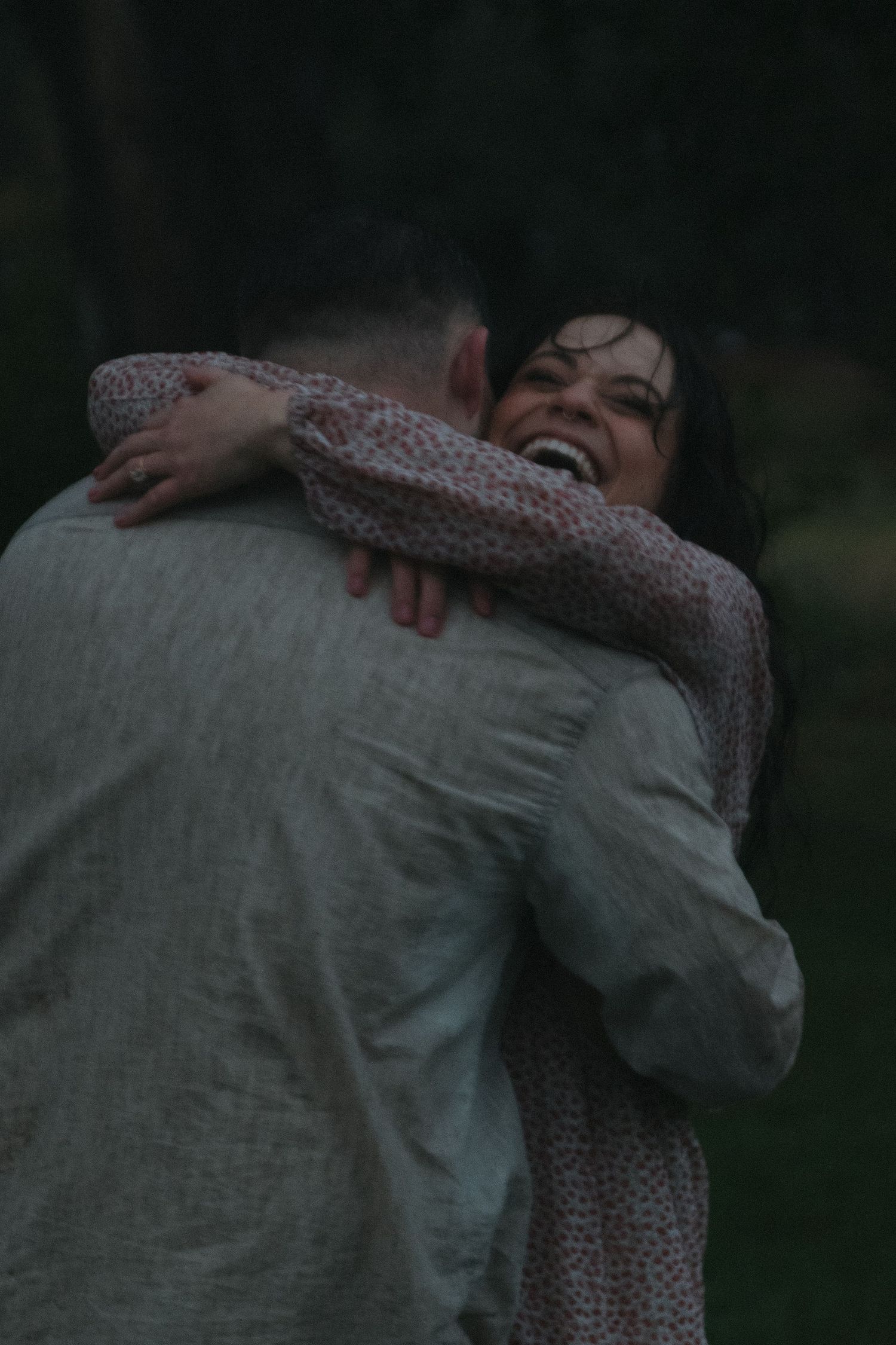 A tender embrace between a couple is captured in soft, moody lighting against a dark background.