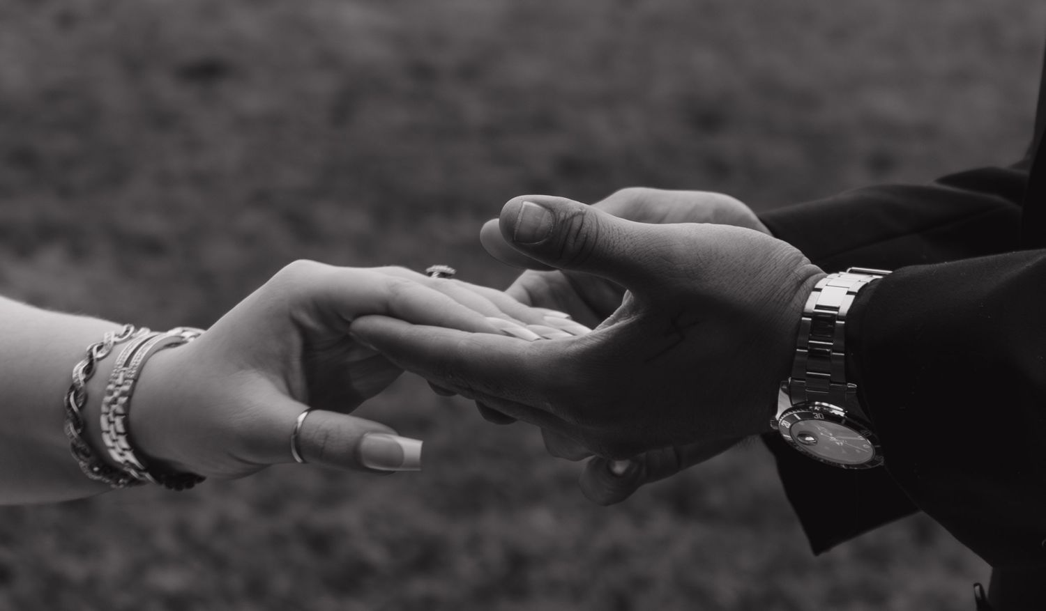 A close-up black and white photo of hands exchanging rings during a wedding ceremony.