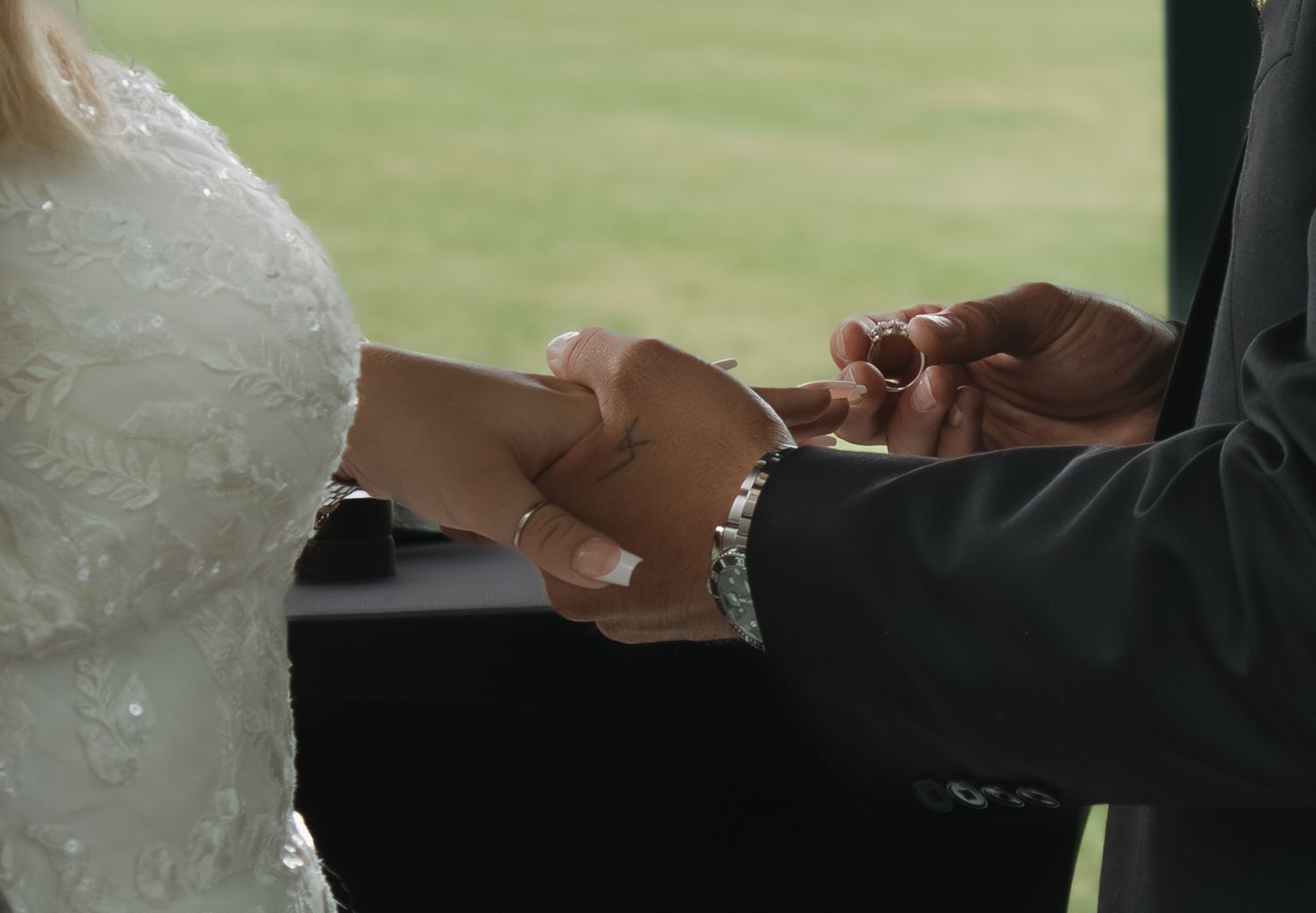 A couple exchanges rings during their outdoor wedding ceremony under a covered pavilion.