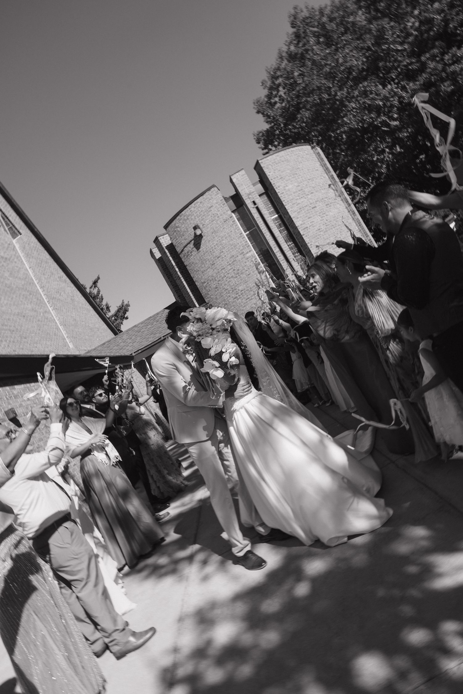 Newlyweds kiss as guests celebrate in a black and white outdoor wedding ceremony recessional photo.