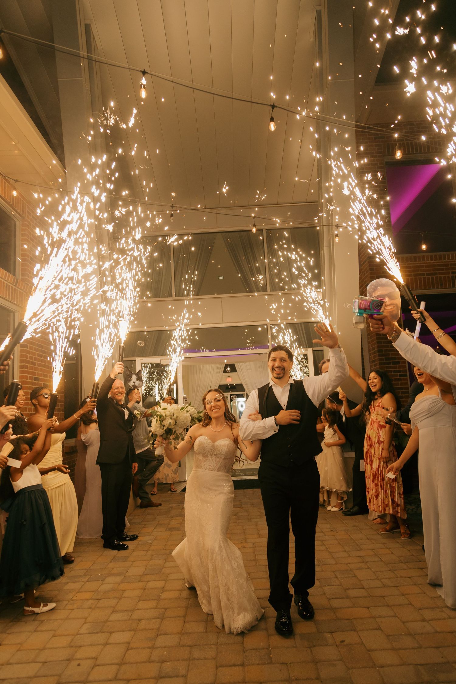 Bride and groom exit wedding reception through dramatic cold sparkler tunnel with guests.