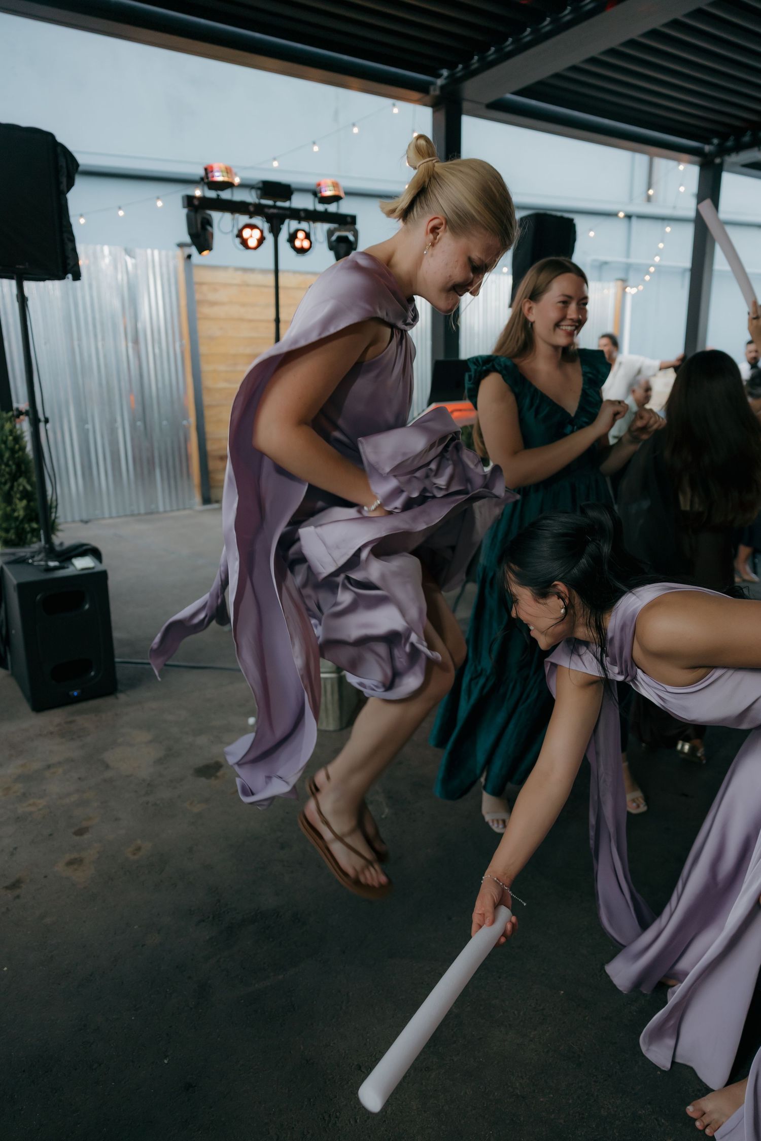 Bridesmaids in purple dresses dancing energetically with glow sticks at lively wedding reception.