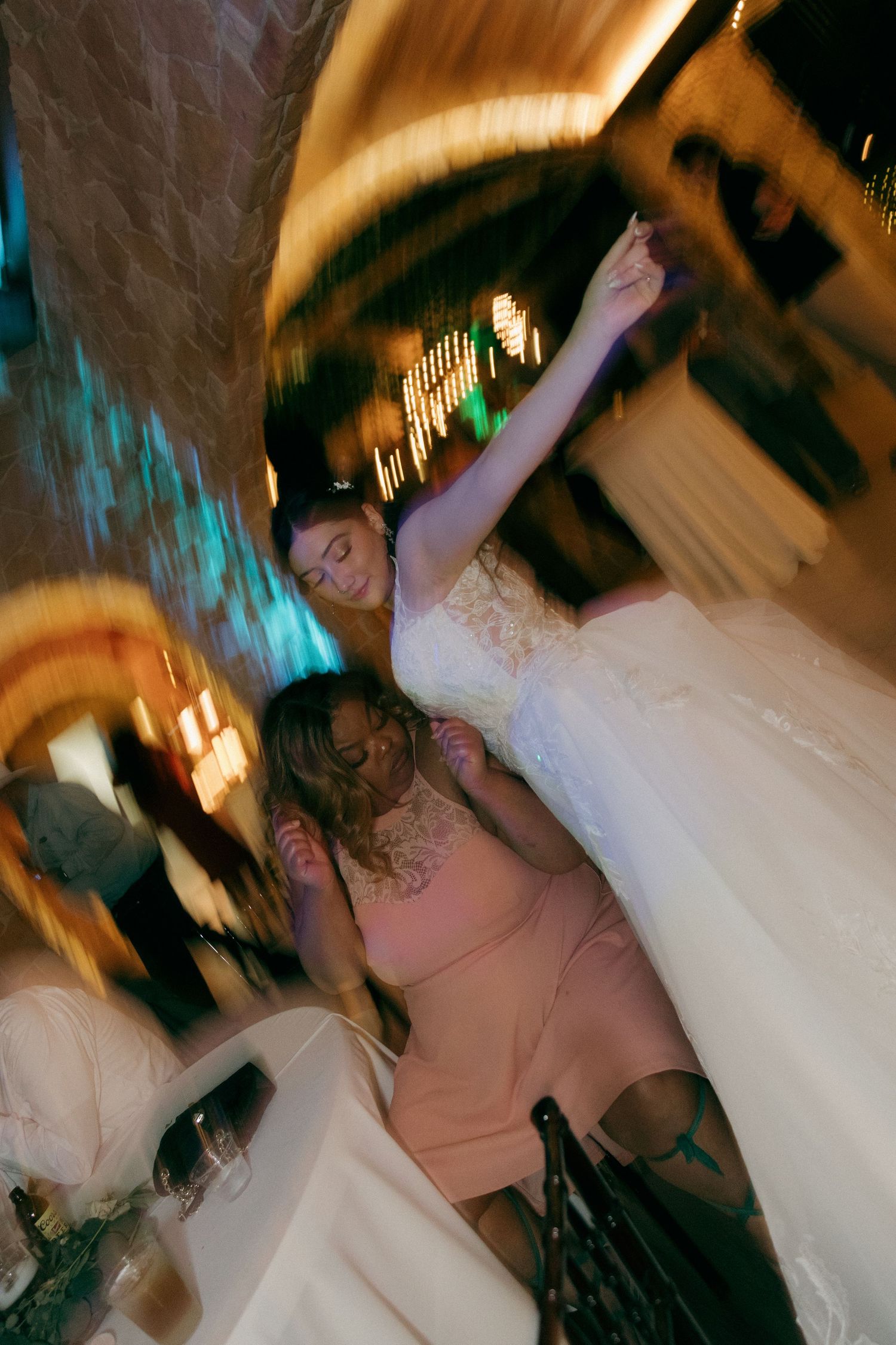 Bride in white gown raises arm while dancing with guests at wedding reception.