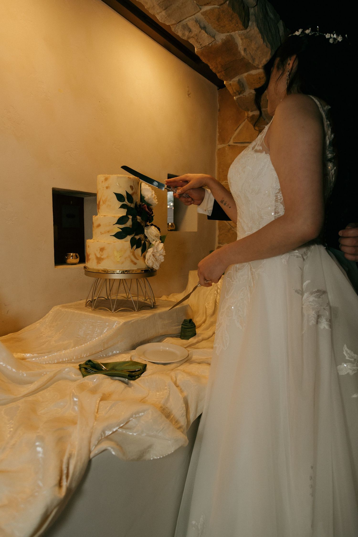 Bride in white gown prepares to cut elegant two-tier wedding cake decorated with florals.