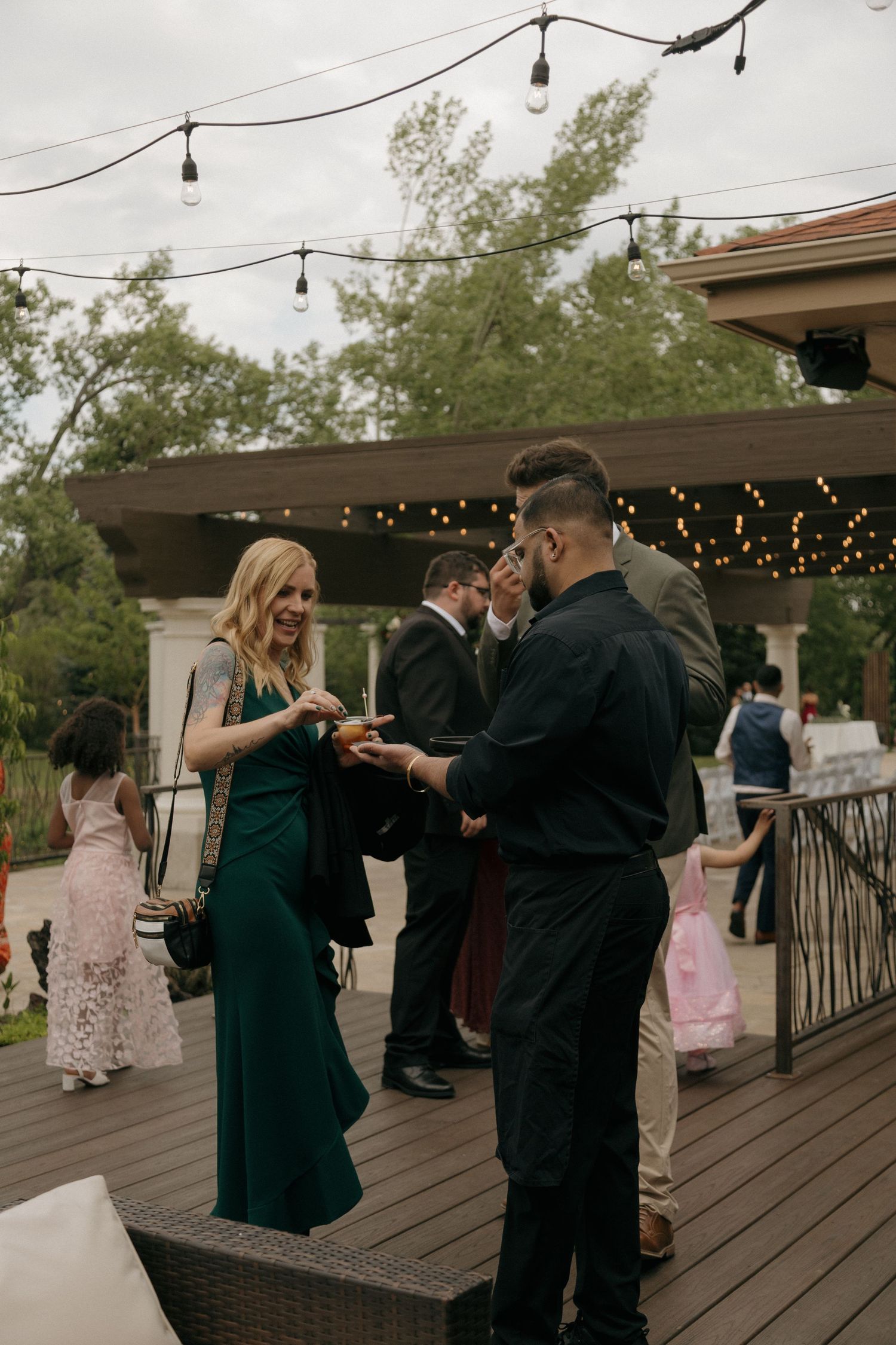 Wedding guests mingle on outdoor deck adorned with string lights at elegant garden reception venue.