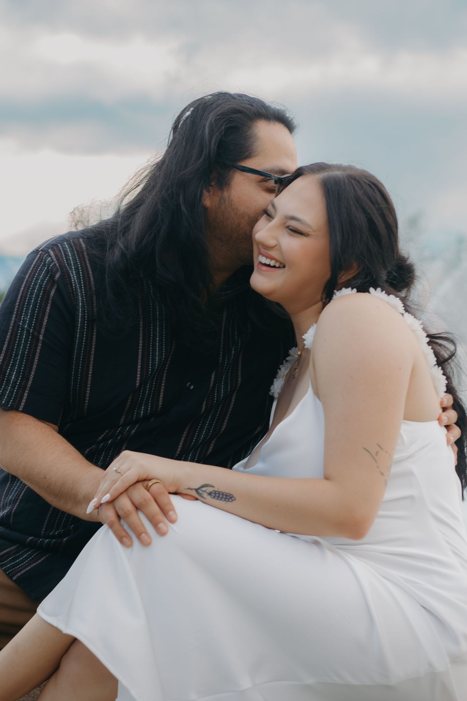 A joyful outdoor embrace against a cloudy sky background.