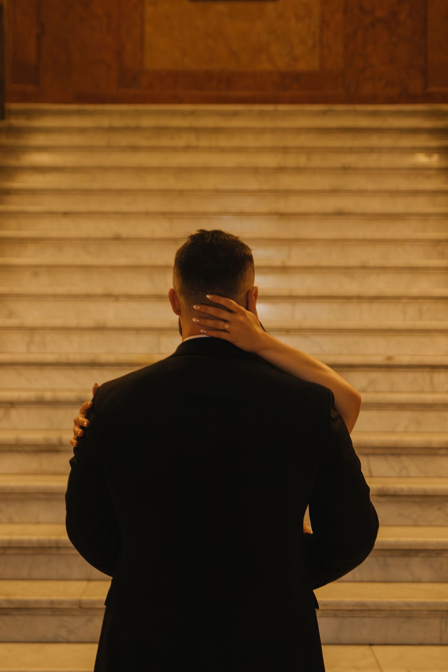 Silhouette of a person in a suit standing on marble steps in warm atmospheric lighting.