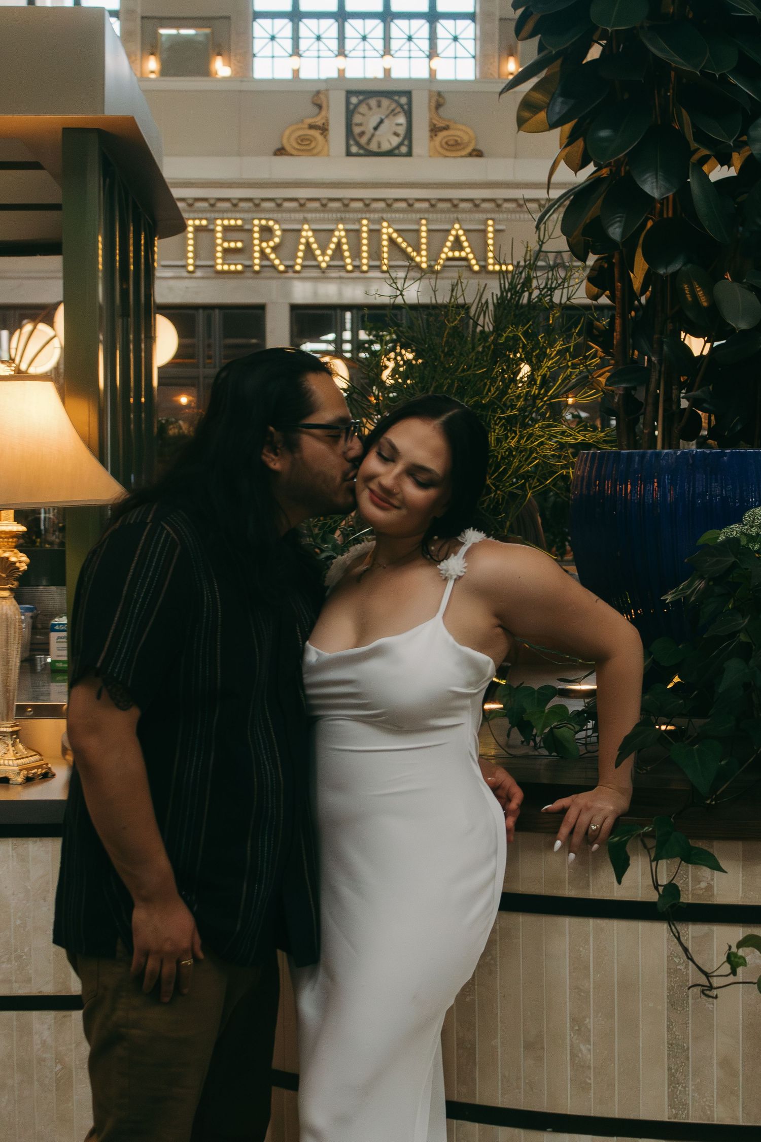 A romantic moment shared between a couple at a transit terminal with decorative plants.