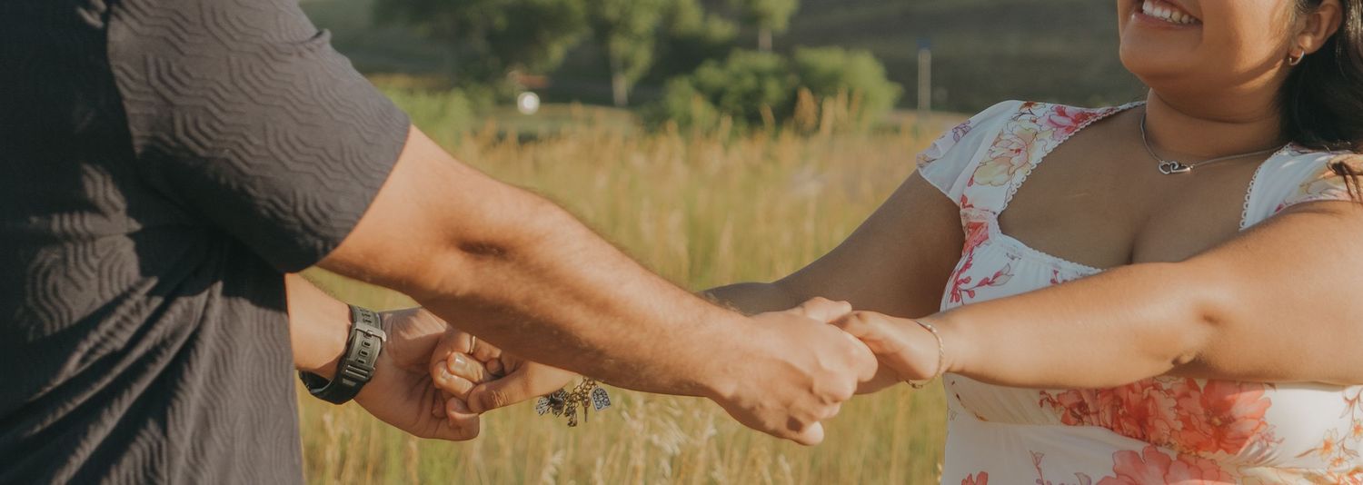 A couple holds hands while sharing a romantic moment in a sunny meadow.