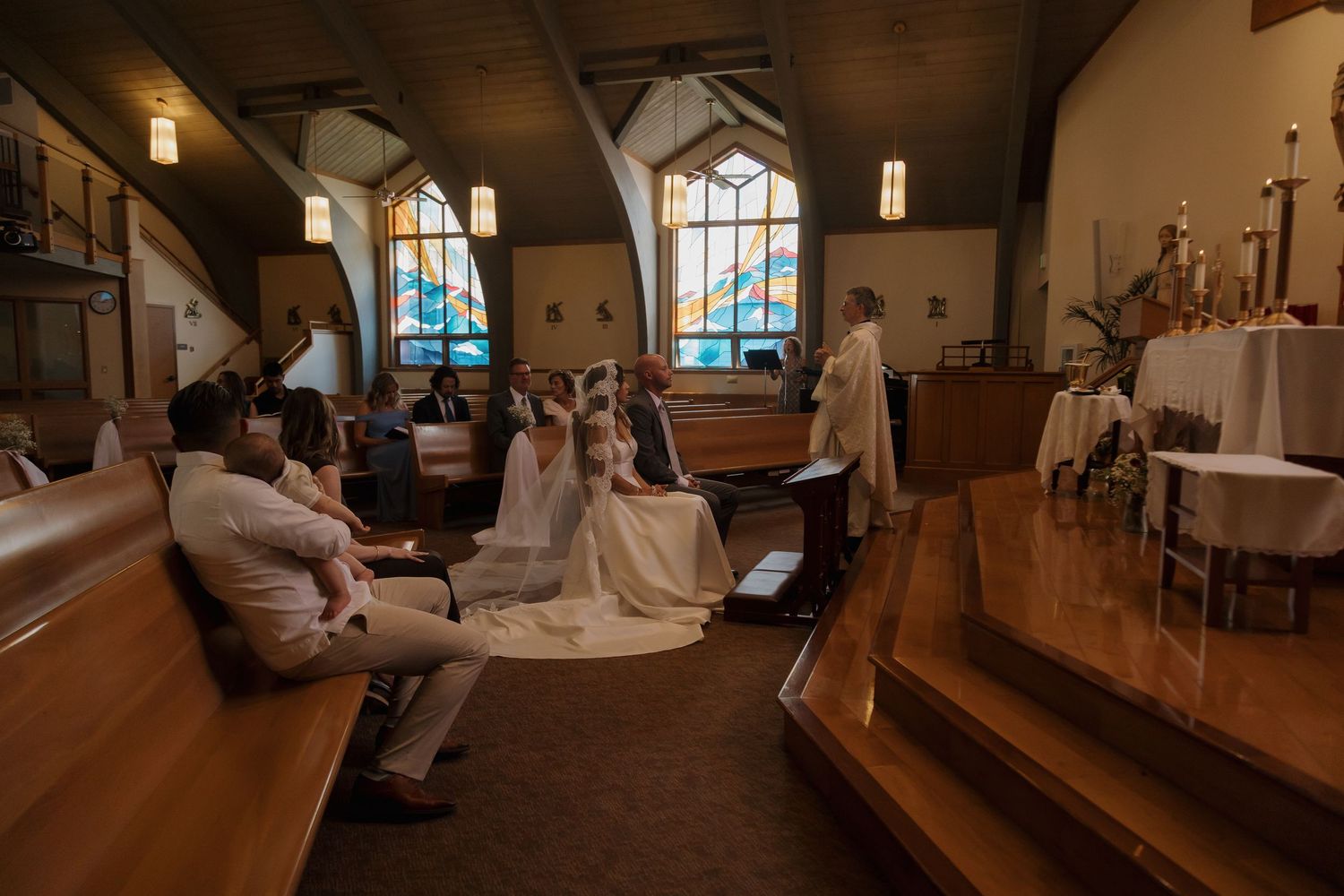 Wide angle view of intimate church wedding ceremony with small congregation in wooden pews.