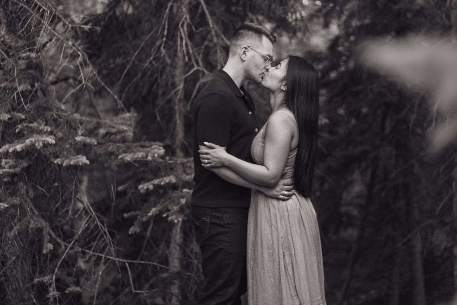 A black and white portrait of a couple embracing in a forest setting.
