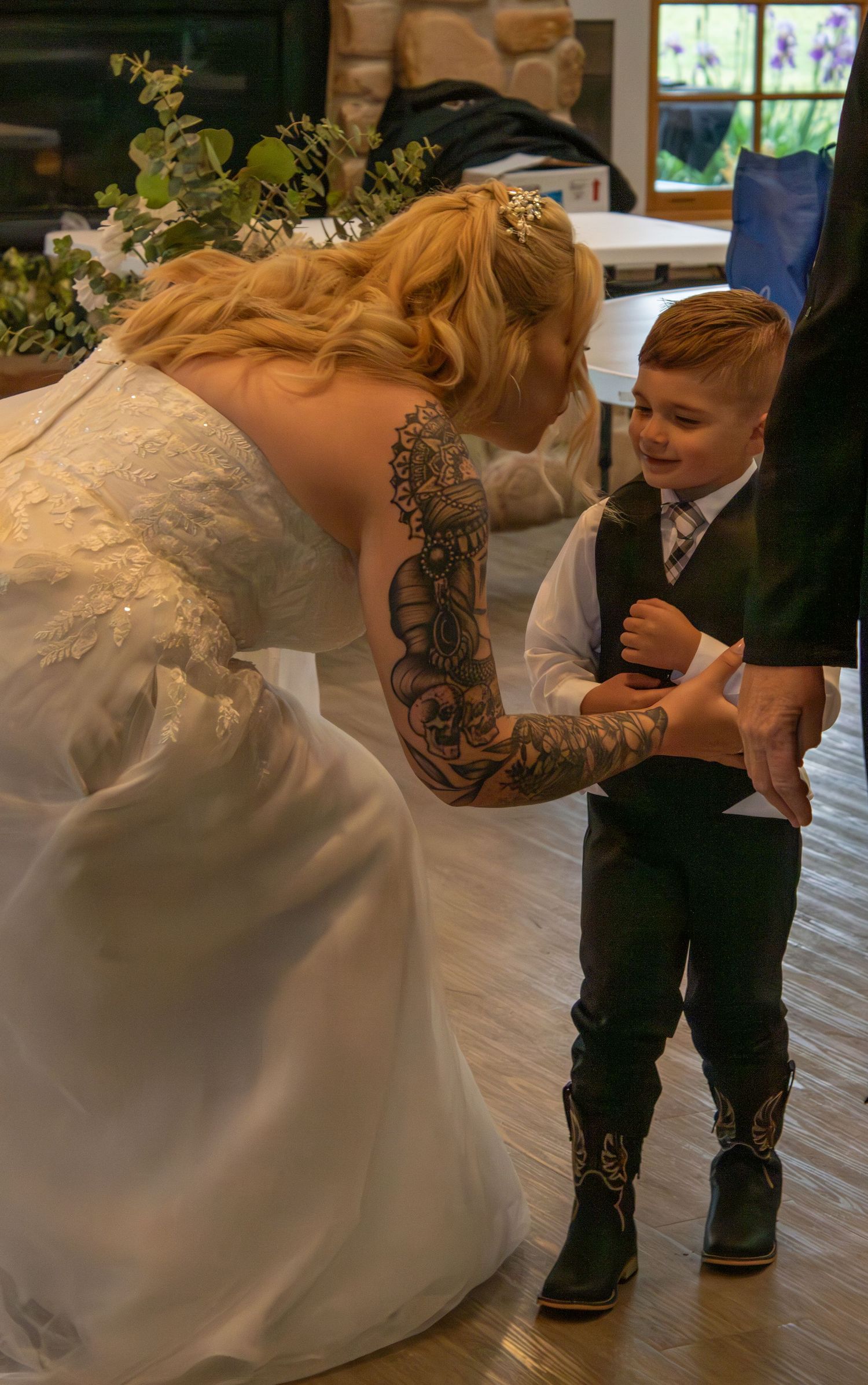 A bride in white dress shows her tattooed arm while interacting with a young guest at the reception.