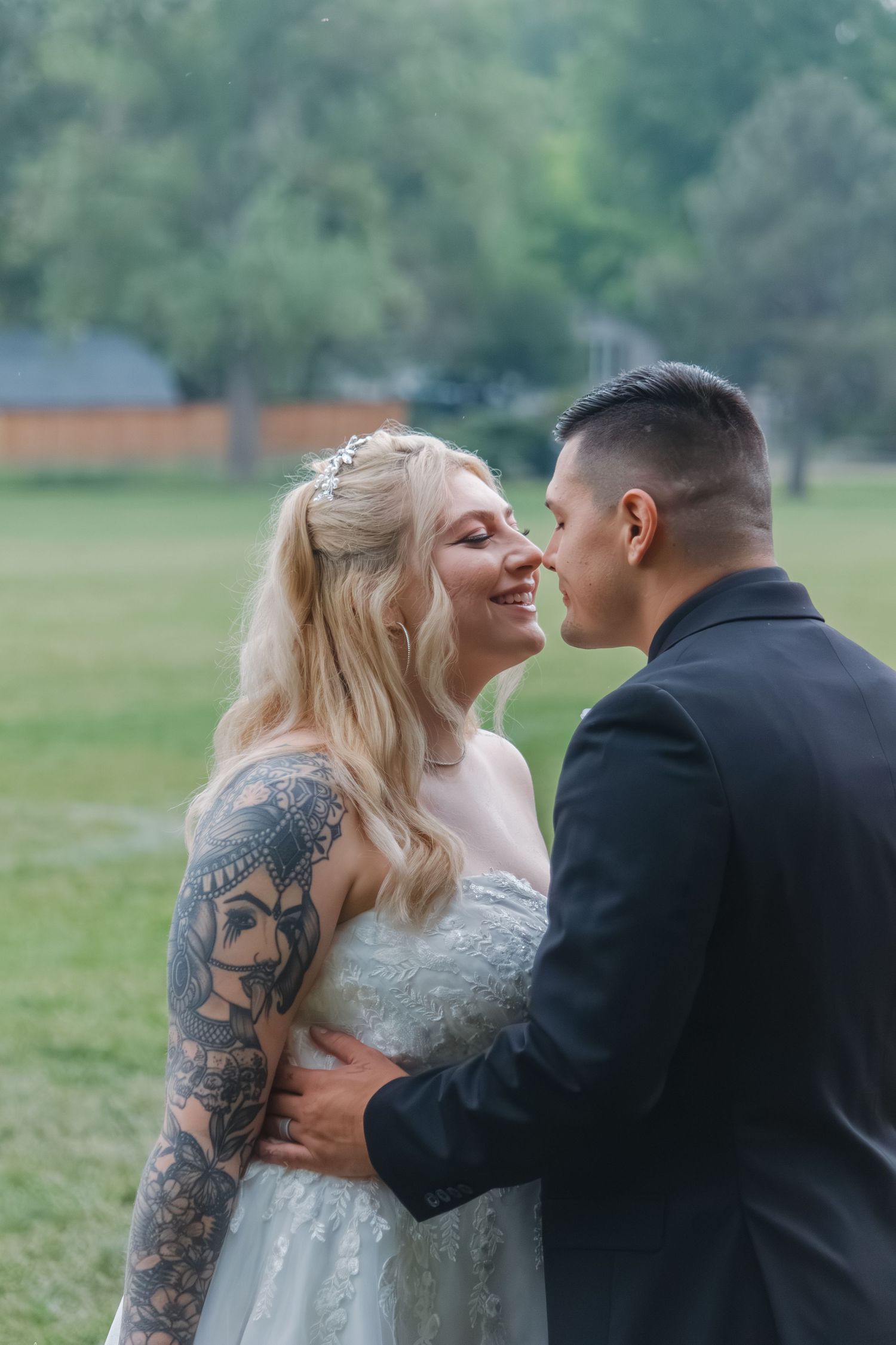 Intimate wedding moment captured outdoors with ornate dress details and tattoo art.