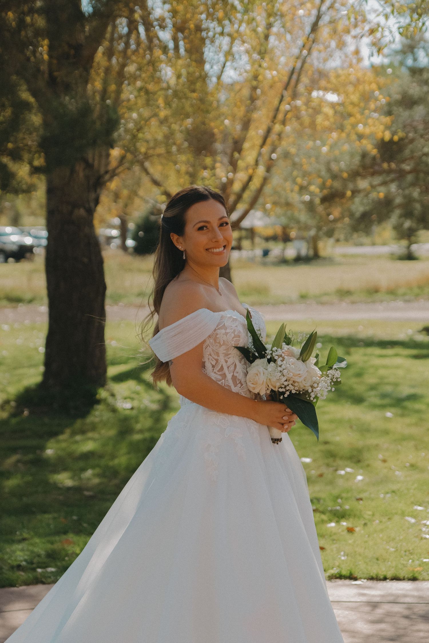 Bride in flowing white ballgown twirls outdoors among autumn trees.