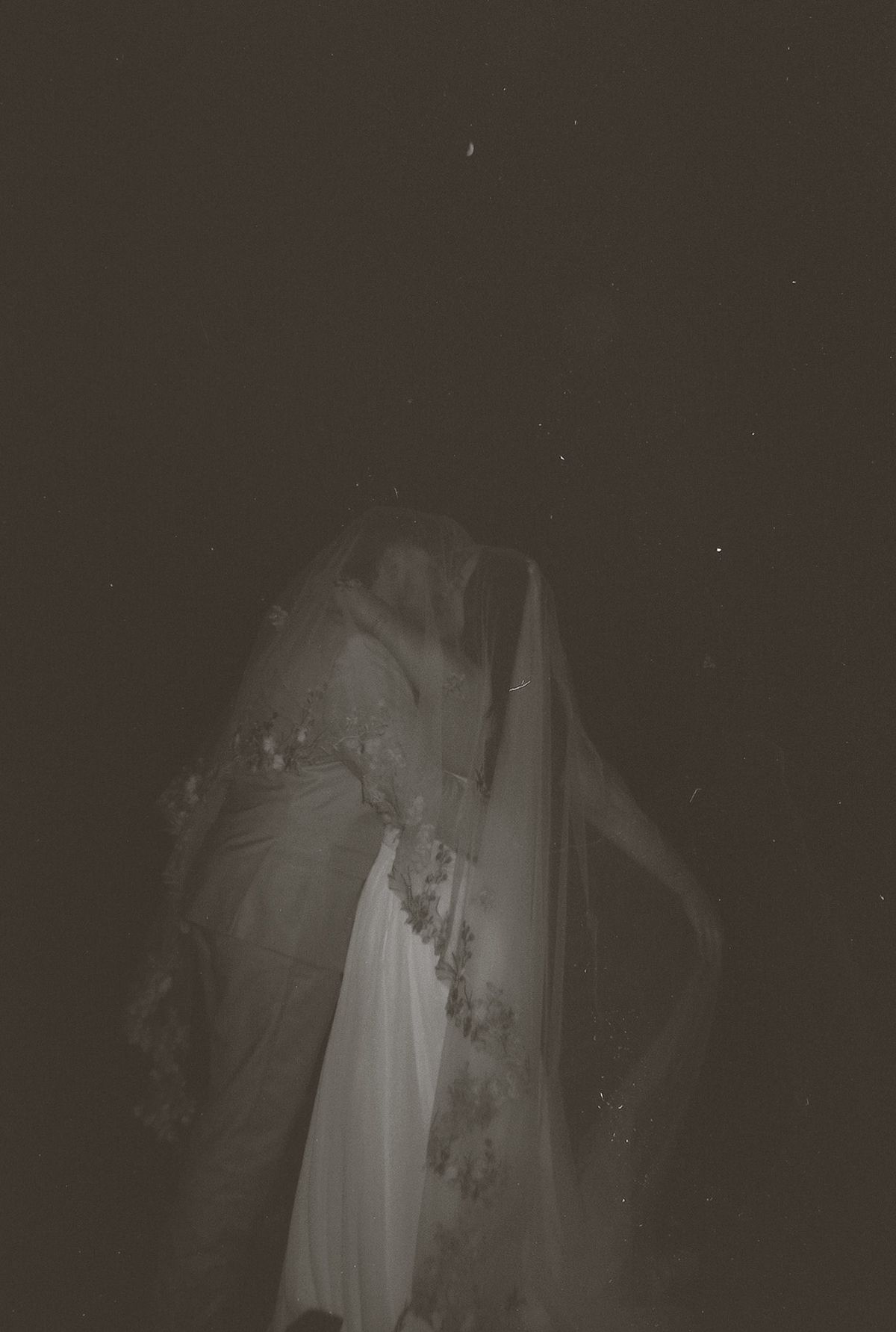 Ethereal dark night photo of bride and groom kissing under the stars with lace veil.
